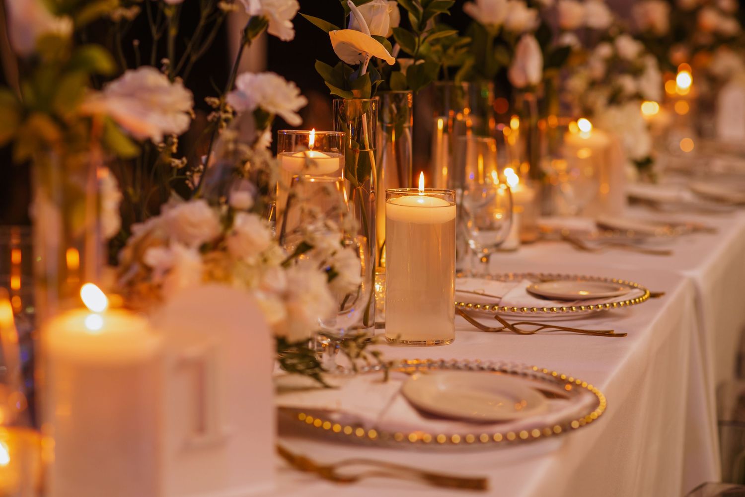 Elegant wedding reception table with candles, white flowers and gold-rimmed place settings.