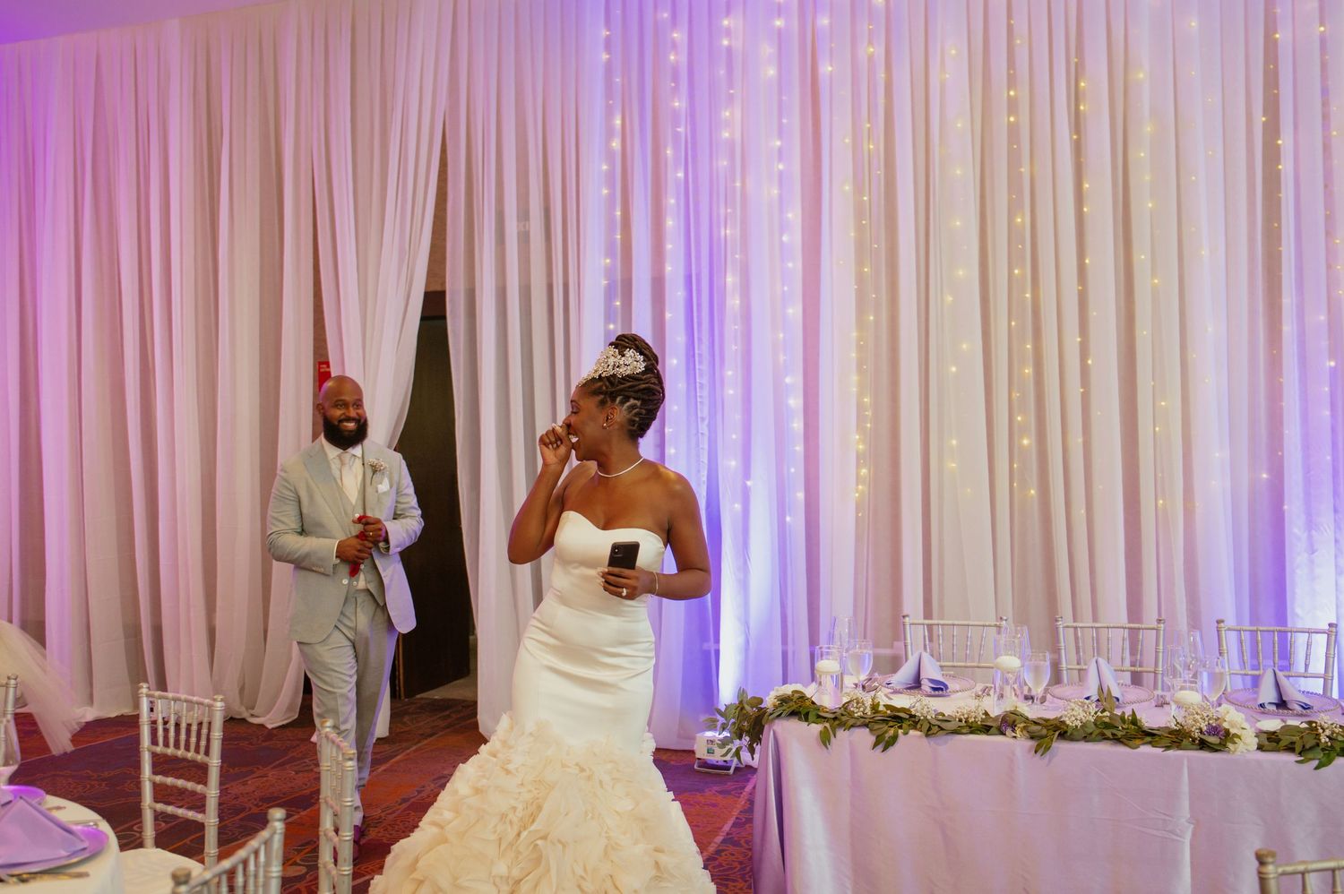 Elegant wedding venue setup with white draping, purple lighting and a bridal gown on display.