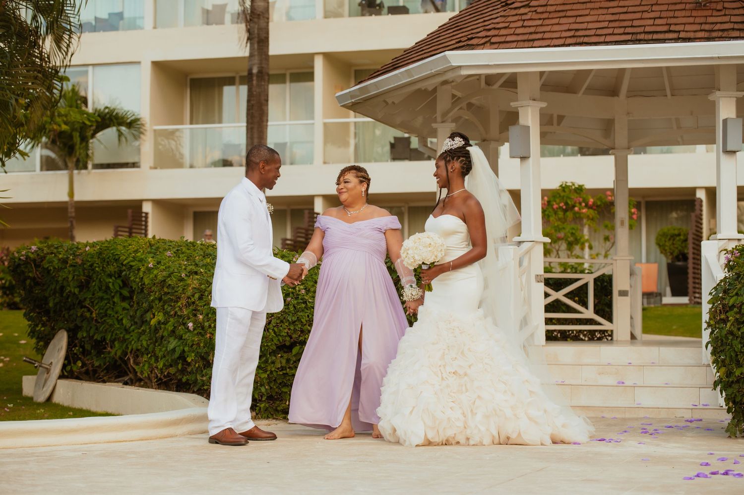 Wedding party members gathered on outdoor terrace with white columns and greenery.