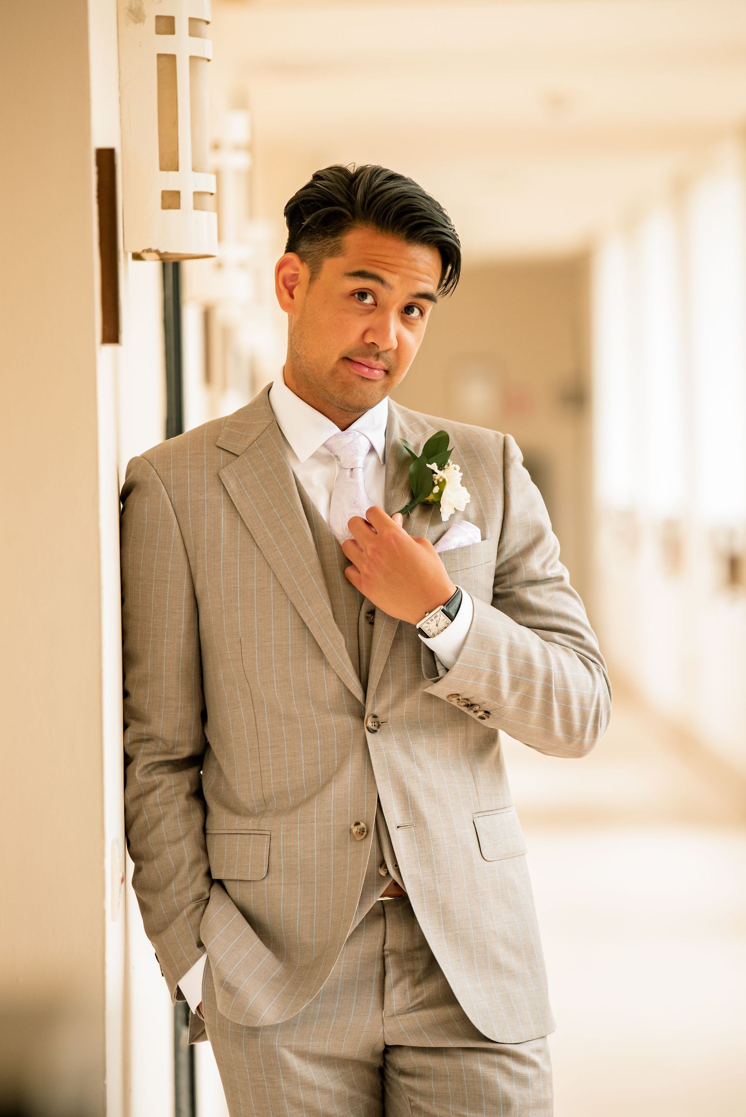 Multiple poses of groom in grey suit against cream colored hallway.