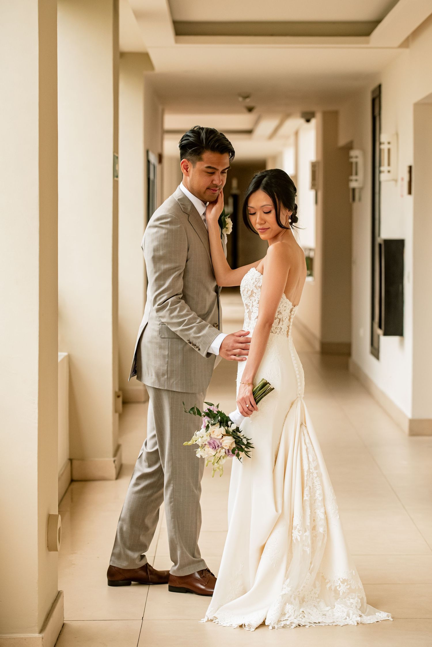 Wedding couple poses in a sunlit corridor with elegant cream walls.