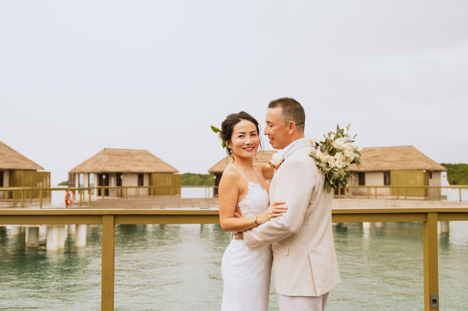 Romantic scene on a wooden boardwalk over water with overwater bungalows in background.