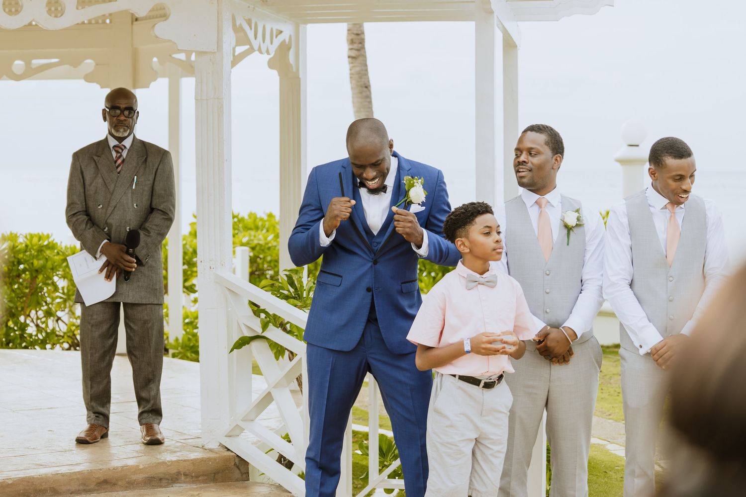 Wedding party members gather on sunny tropical terrace for celebration photos.