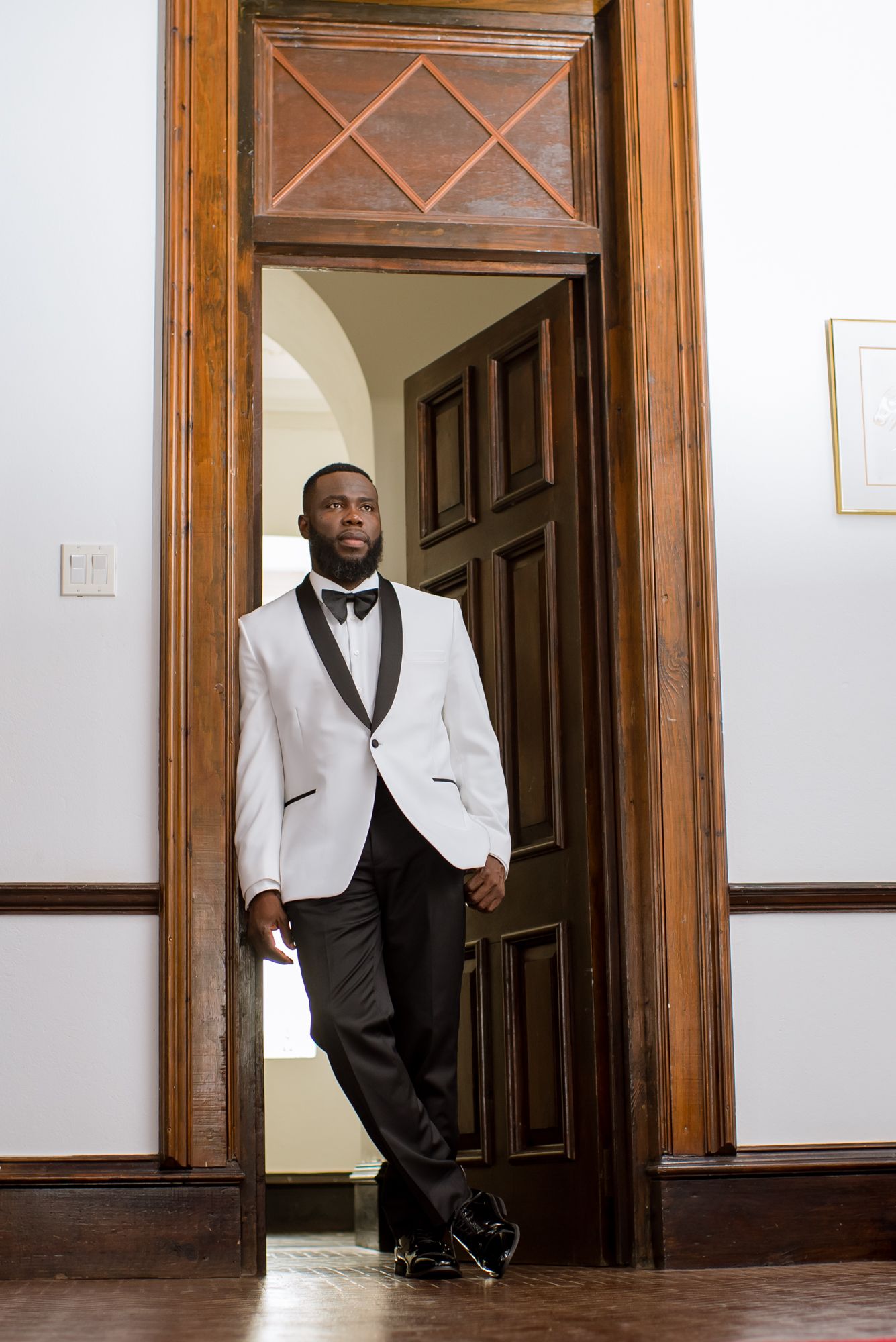 A person in a white tuxedo jacket standing in a doorway with wooden trim.