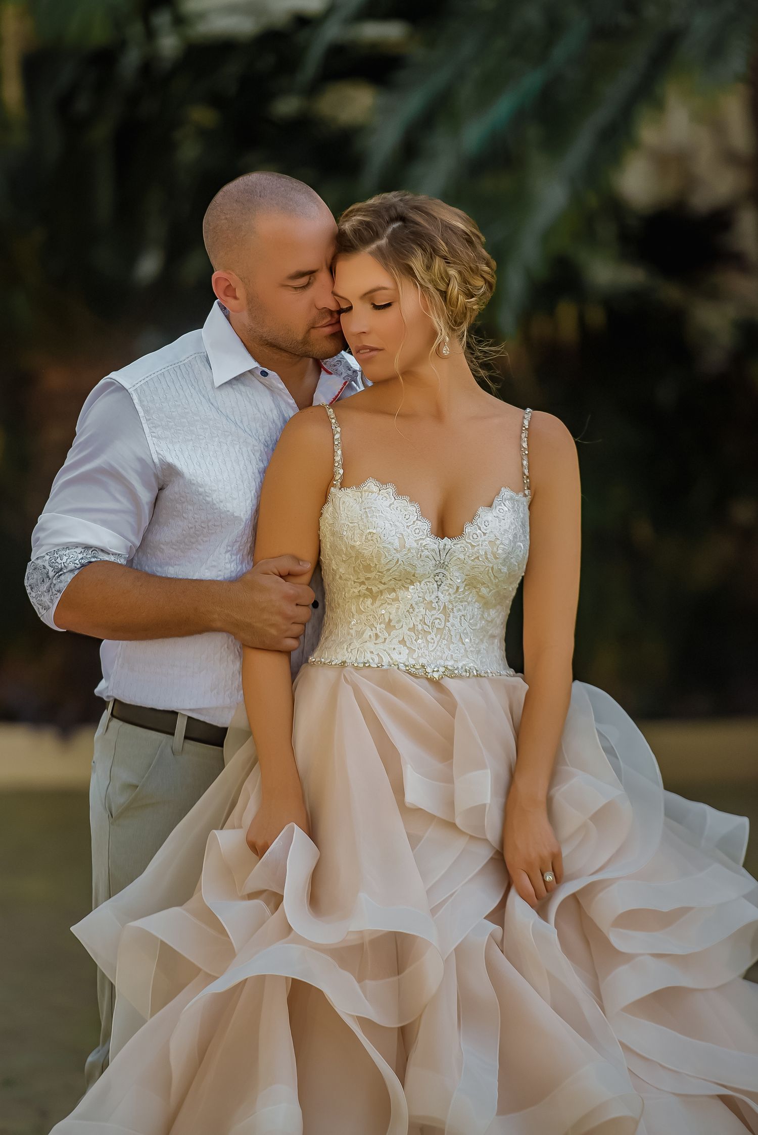 A romantic couple in wedding attire share intimate moments during an outdoor photo session in natural lighting.
