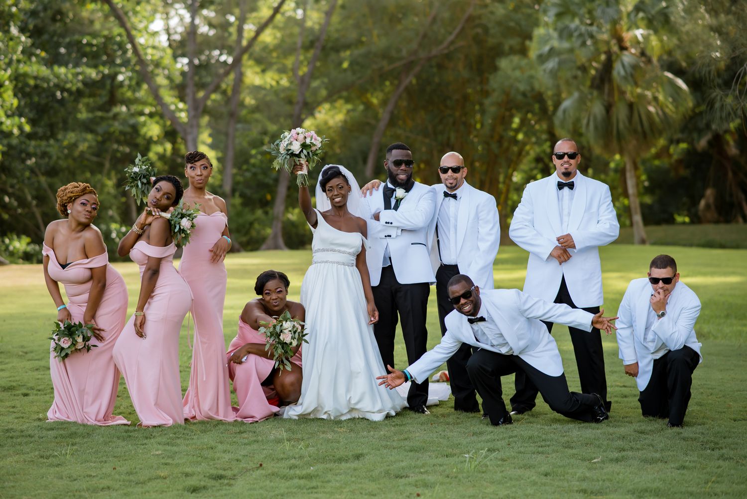 Wedding party poses casually on grass during outdoor photo session.
