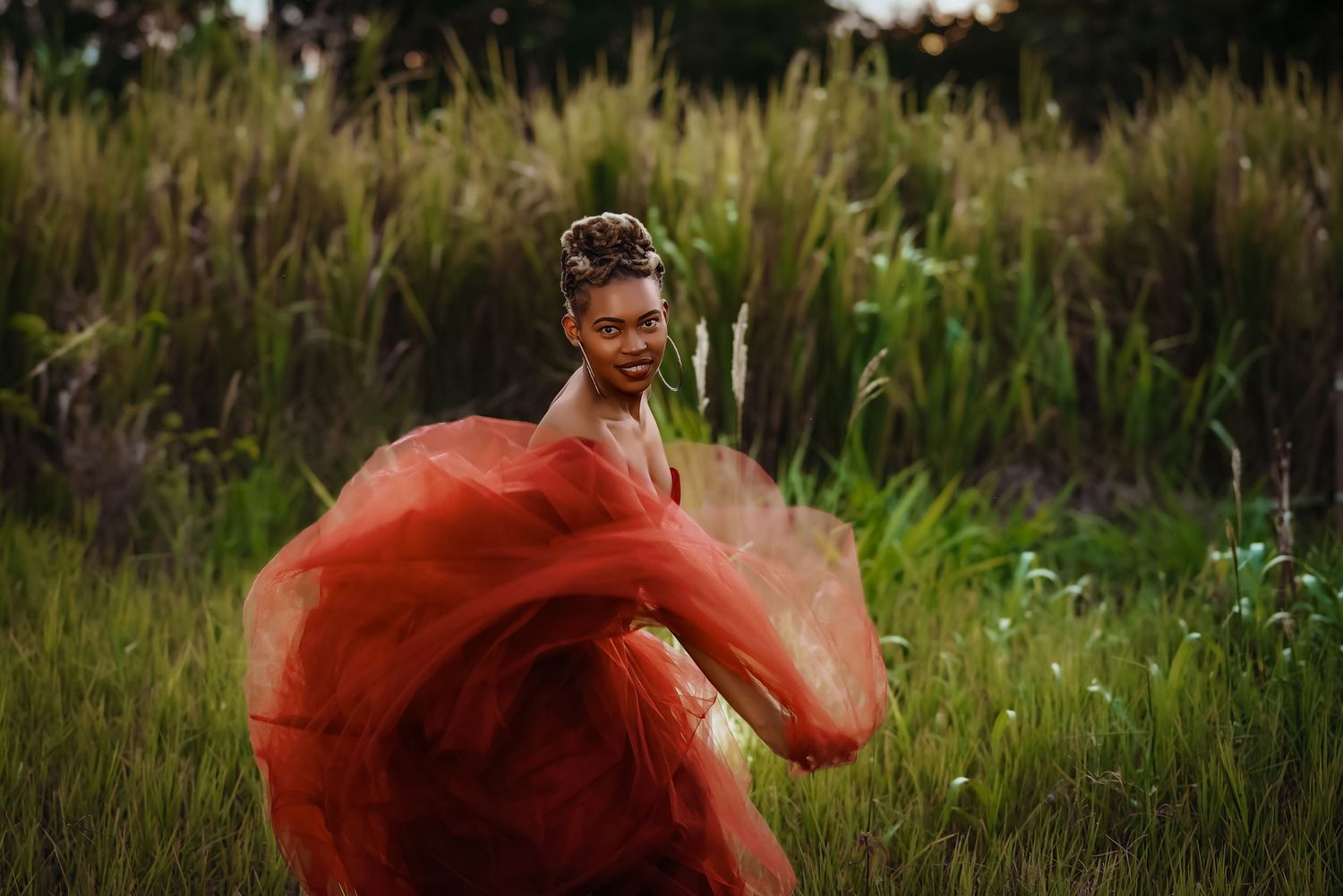 Dramatic red dress billows in the wind among tall grasses at golden hour.