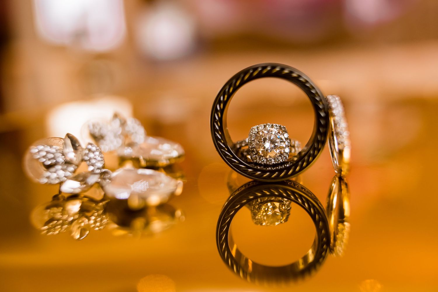 Wedding rings with intricate black rope design detail photographed on reflective surface.