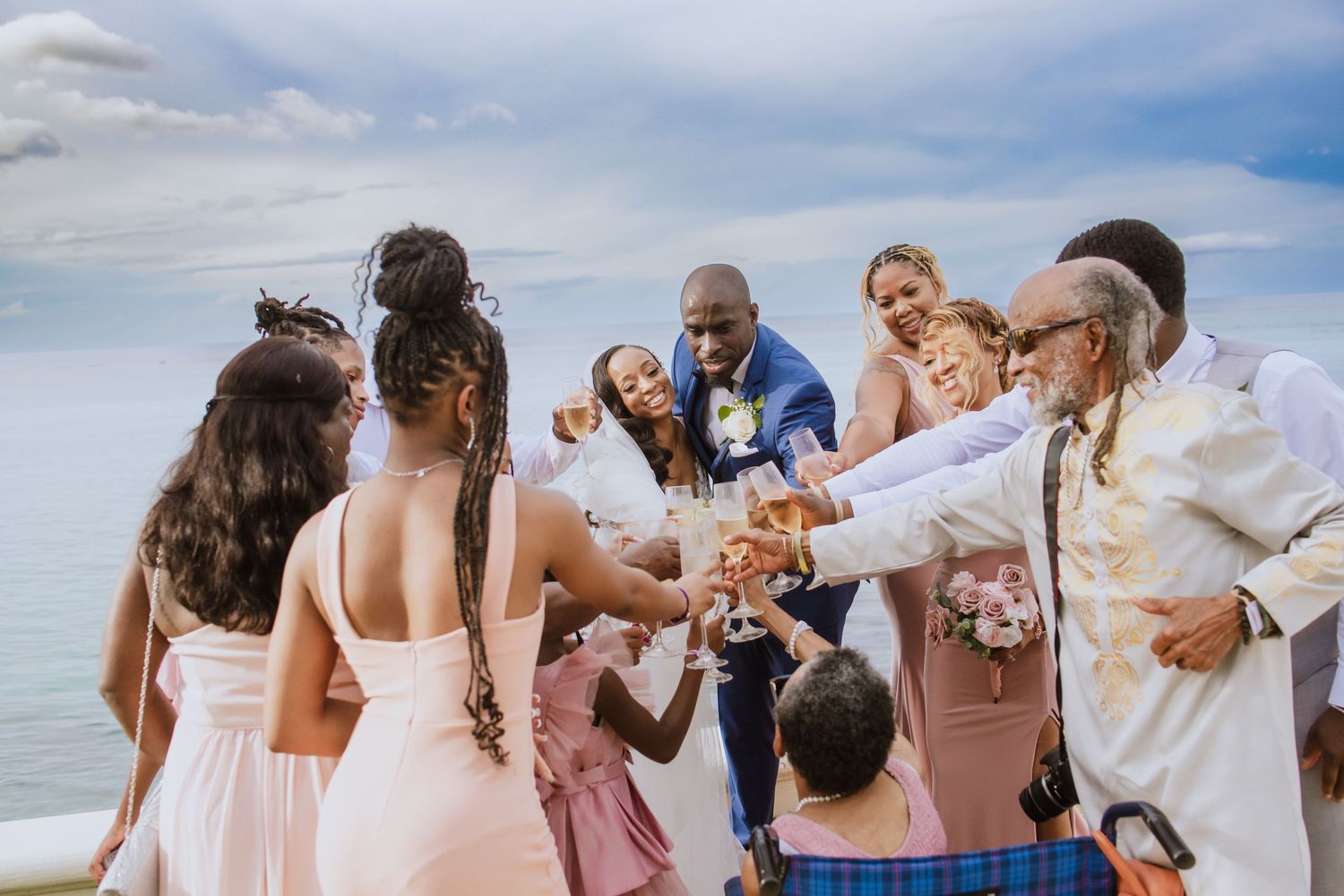 Wedding party celebrates with champagne by the ocean on a cloudy day.