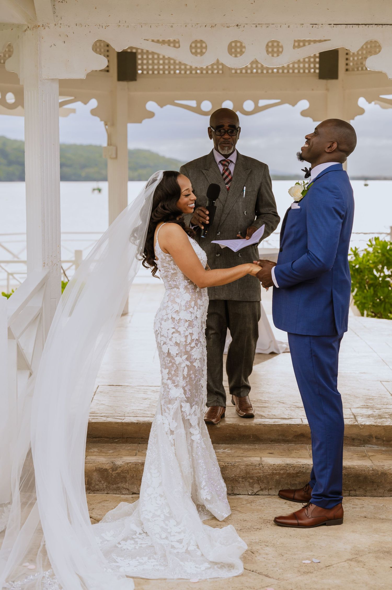 A wedding ceremony unfolds in an ornate white gazebo overlooking a scenic waterfront.