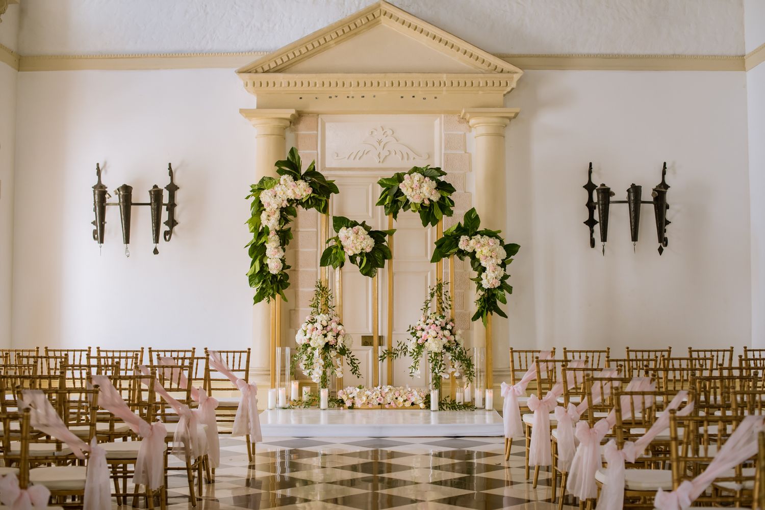 Classic white wedding chapel interior with gold chiavari chairs and decorative floral arrangements.
