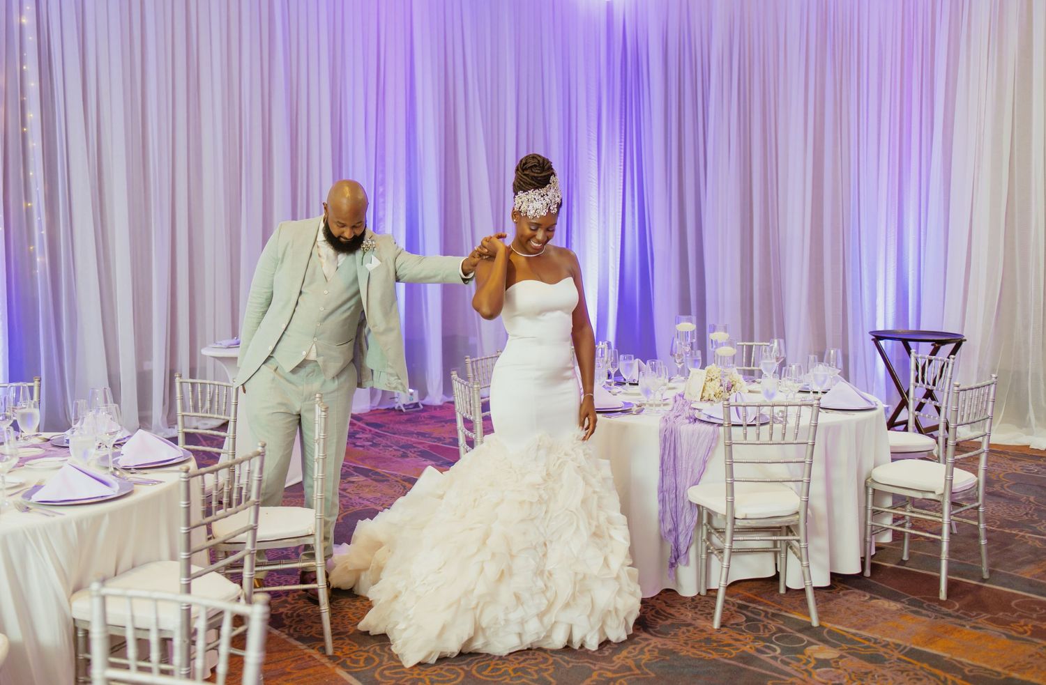 Wedding ballroom with white drapery, purple accent lighting and elegant table settings.