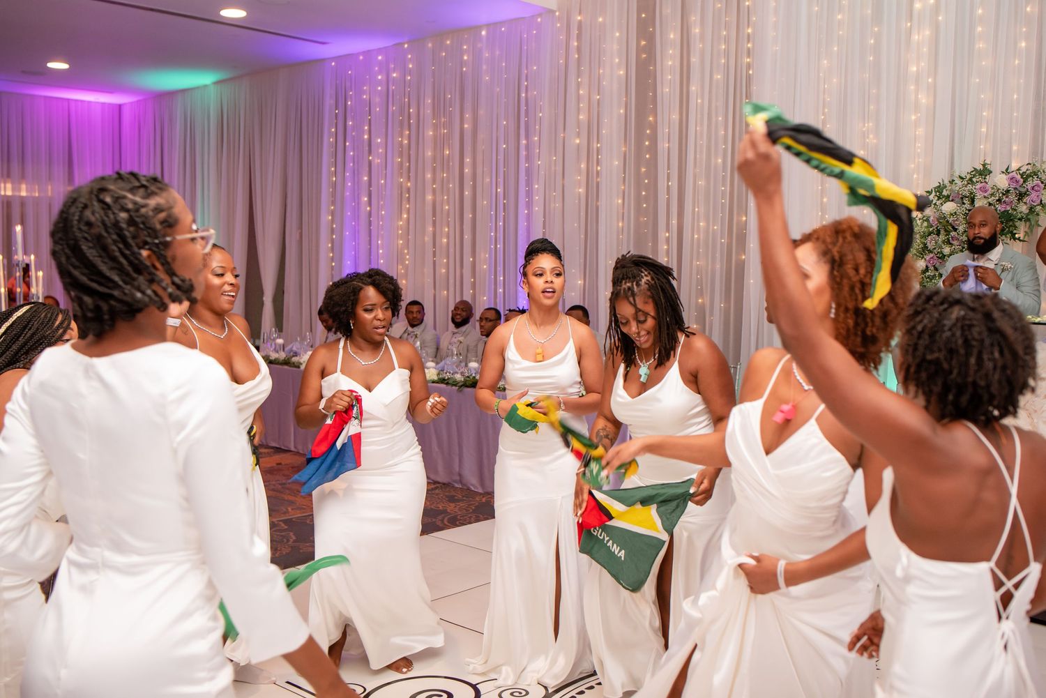 Wedding party dancing and celebrating with colorful sashes in an elegant reception venue.