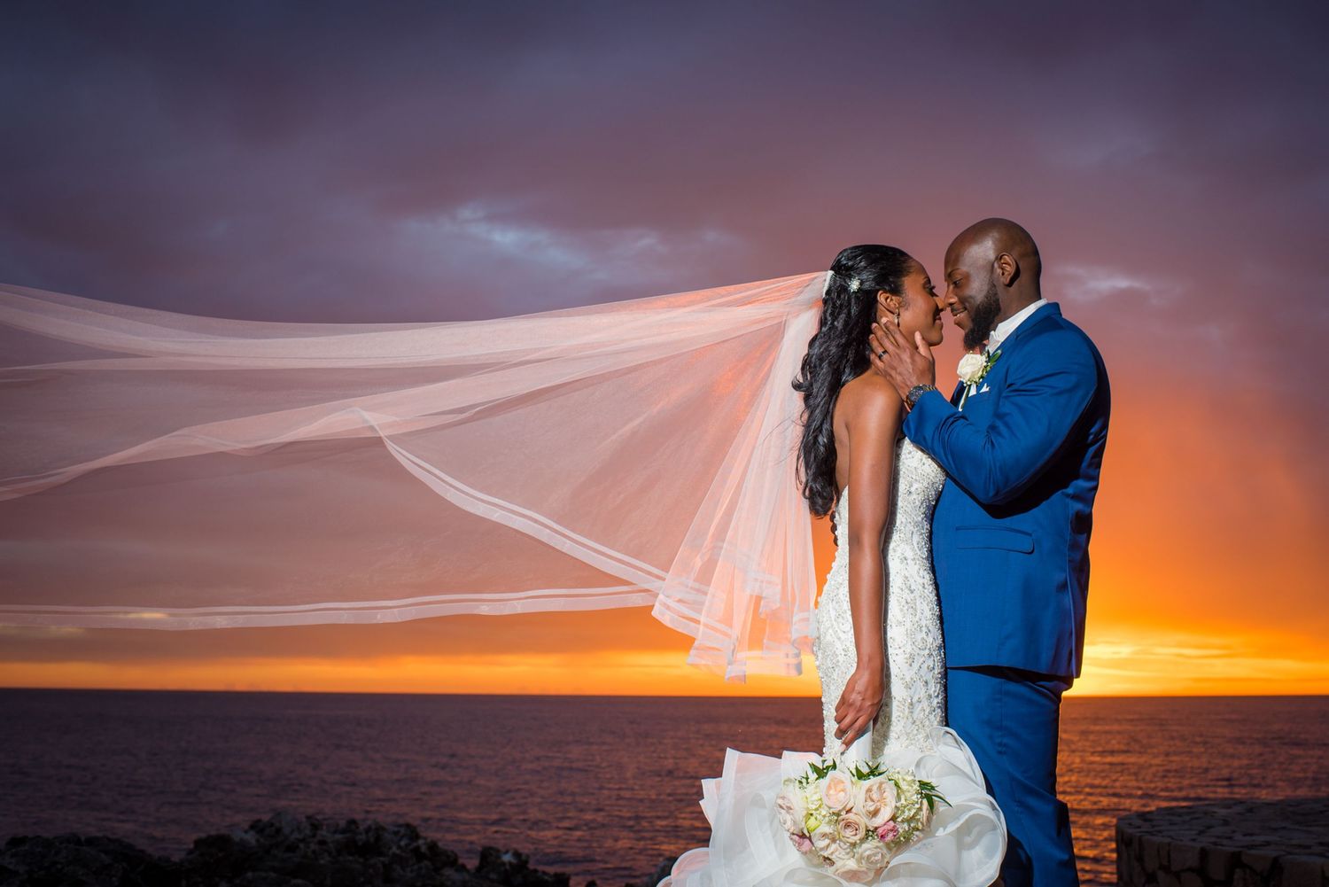 Beachside wedding couple embracing against dramatic orange and purple sunset sky.