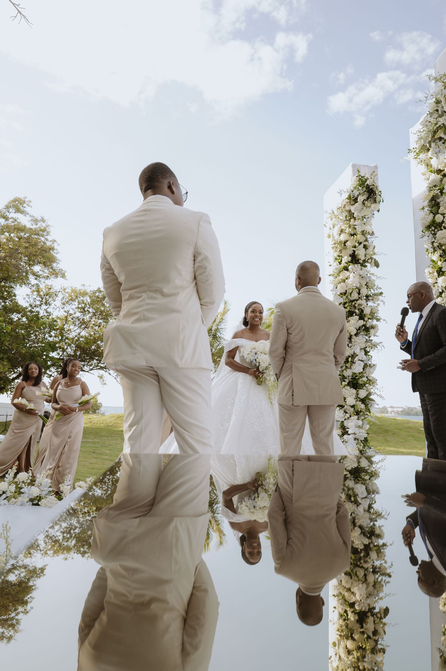 Wedding ceremony under floral arch with guests in cream and white attire.