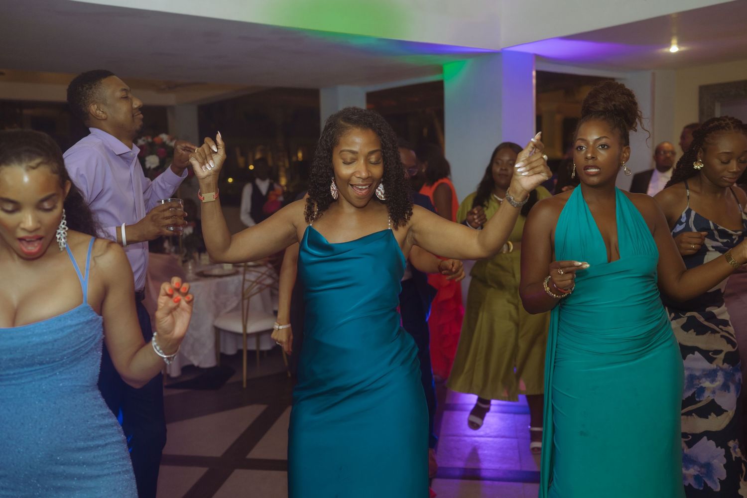 Wedding guests in coordinated teal dresses dancing at reception party.