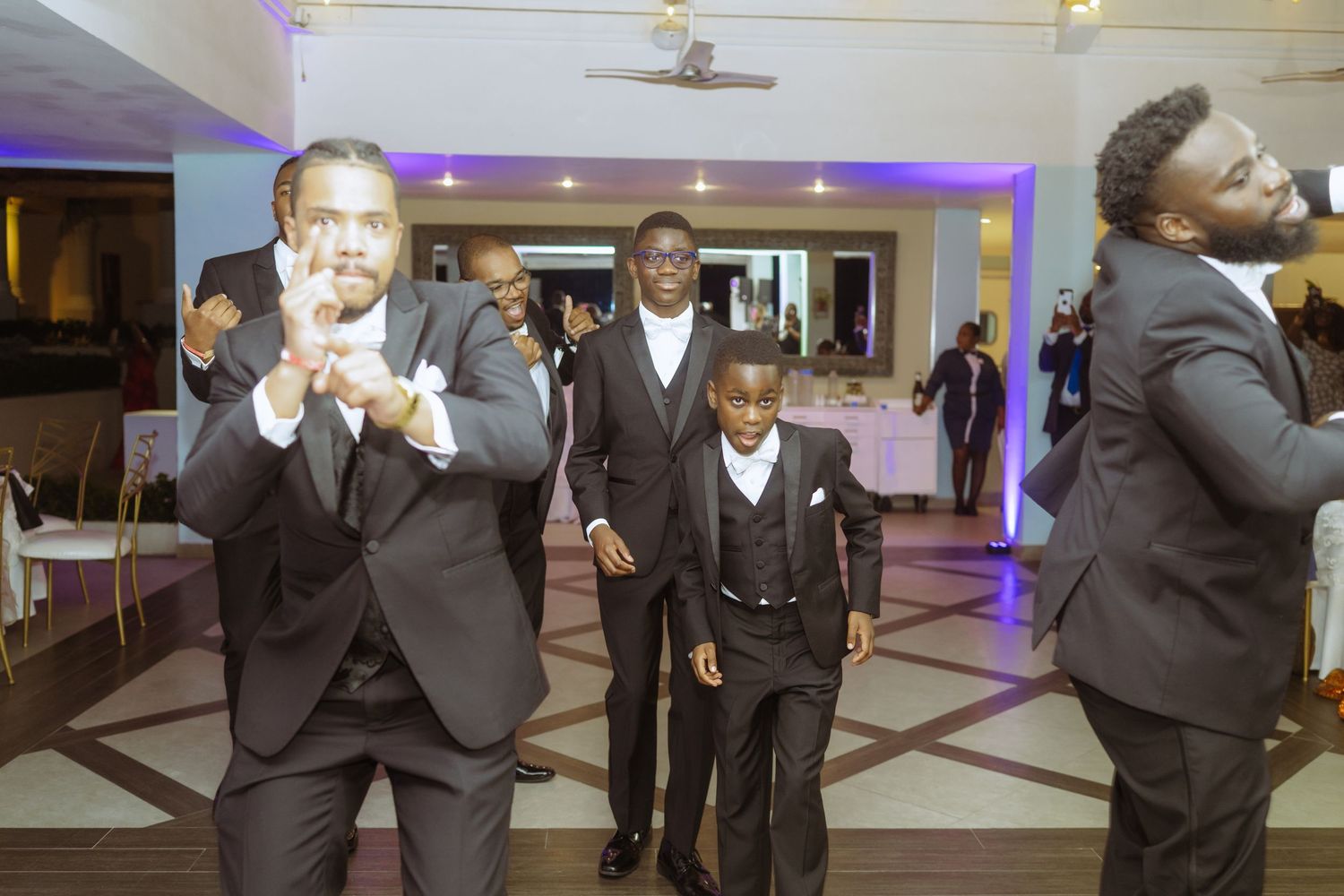 Groomsmen in black suits posing and laughing together at wedding celebration.