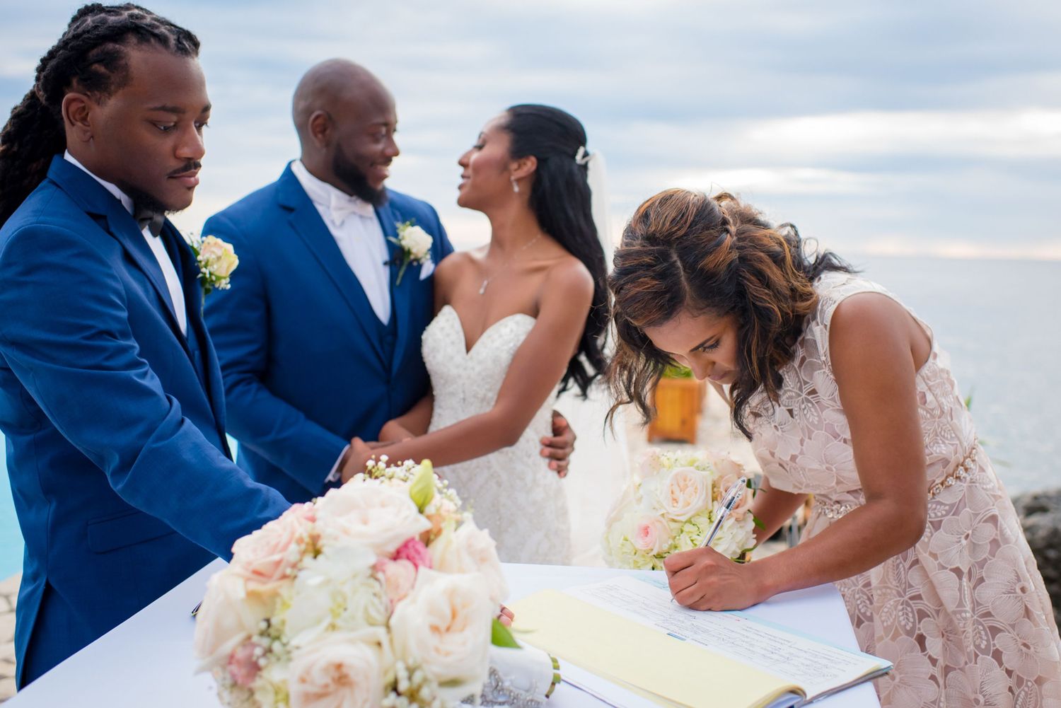 Elegant beach wedding celebration with guests in formal attire and floral decorations.