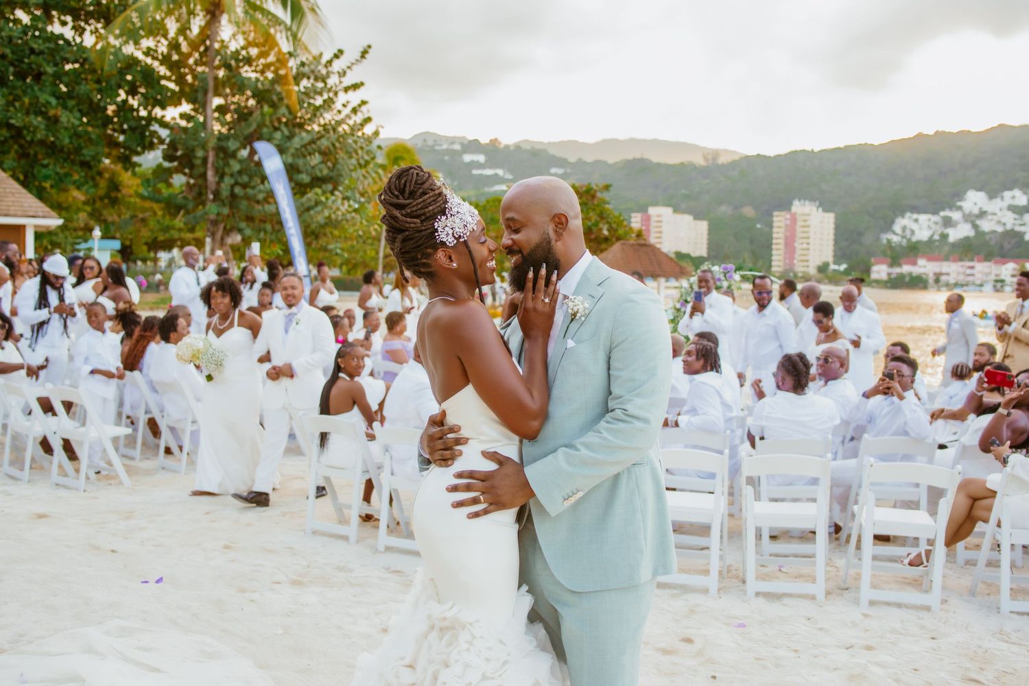 Beach wedding setup with white chairs and floral decorations against a coastal backdrop.