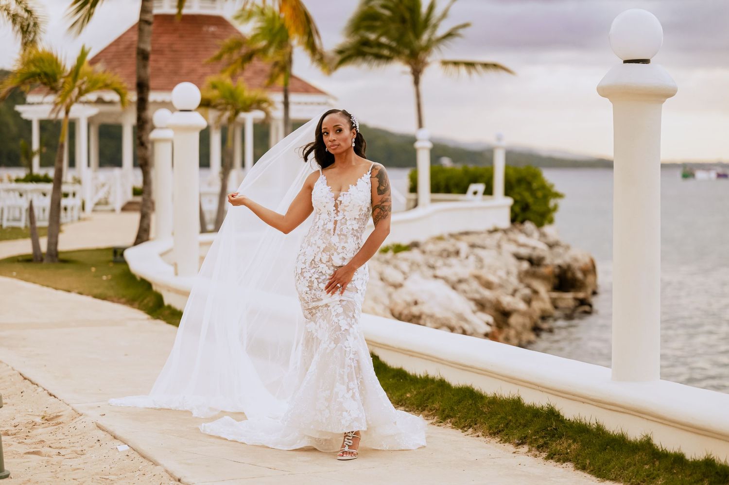 A tropical wedding photoshoot featuring a waterfront walkway and swaying palm trees.