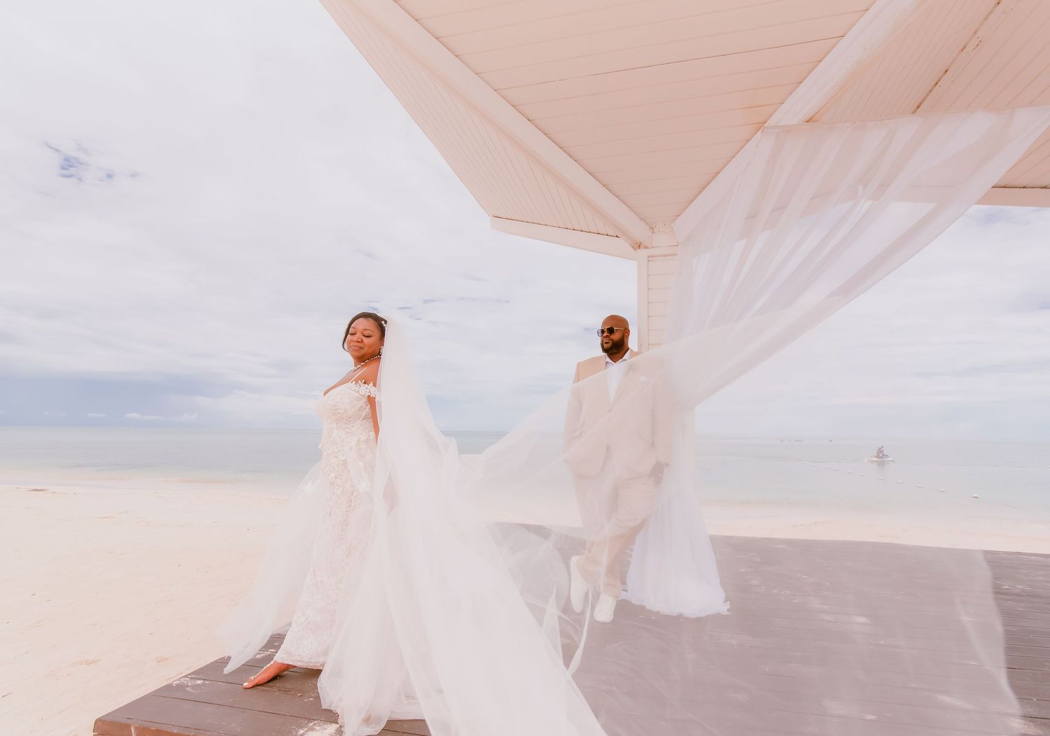 Flowing white fabric creates ethereal movement against pale sky in beach photoshoot.