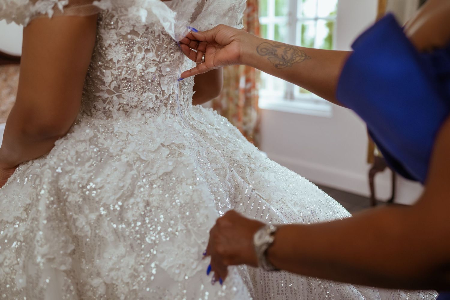 Wedding dress details being adjusted with delicate lace and beading in natural light.