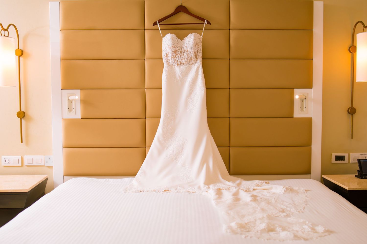 Wedding dress hanging in hotel room with warm lighting.