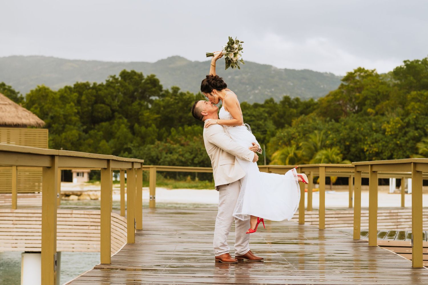 A couple shares an intimate moment on a wooden pier with mountains in the background.