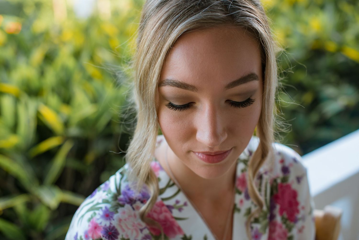 Close-up of bridal makeup and hair styling with floral background.