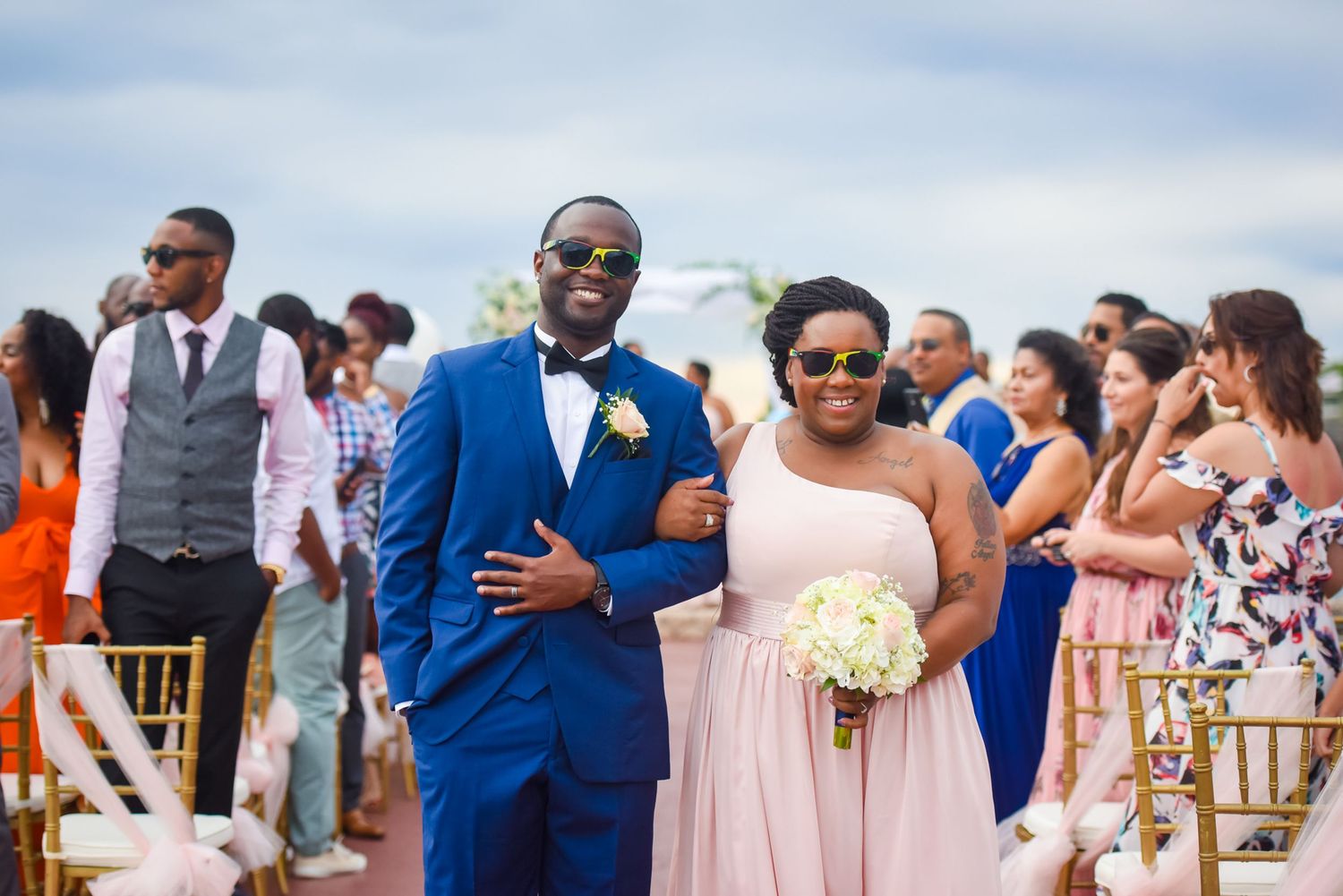 Wedding party in coordinated blue and pink attire celebrating at beach venue.