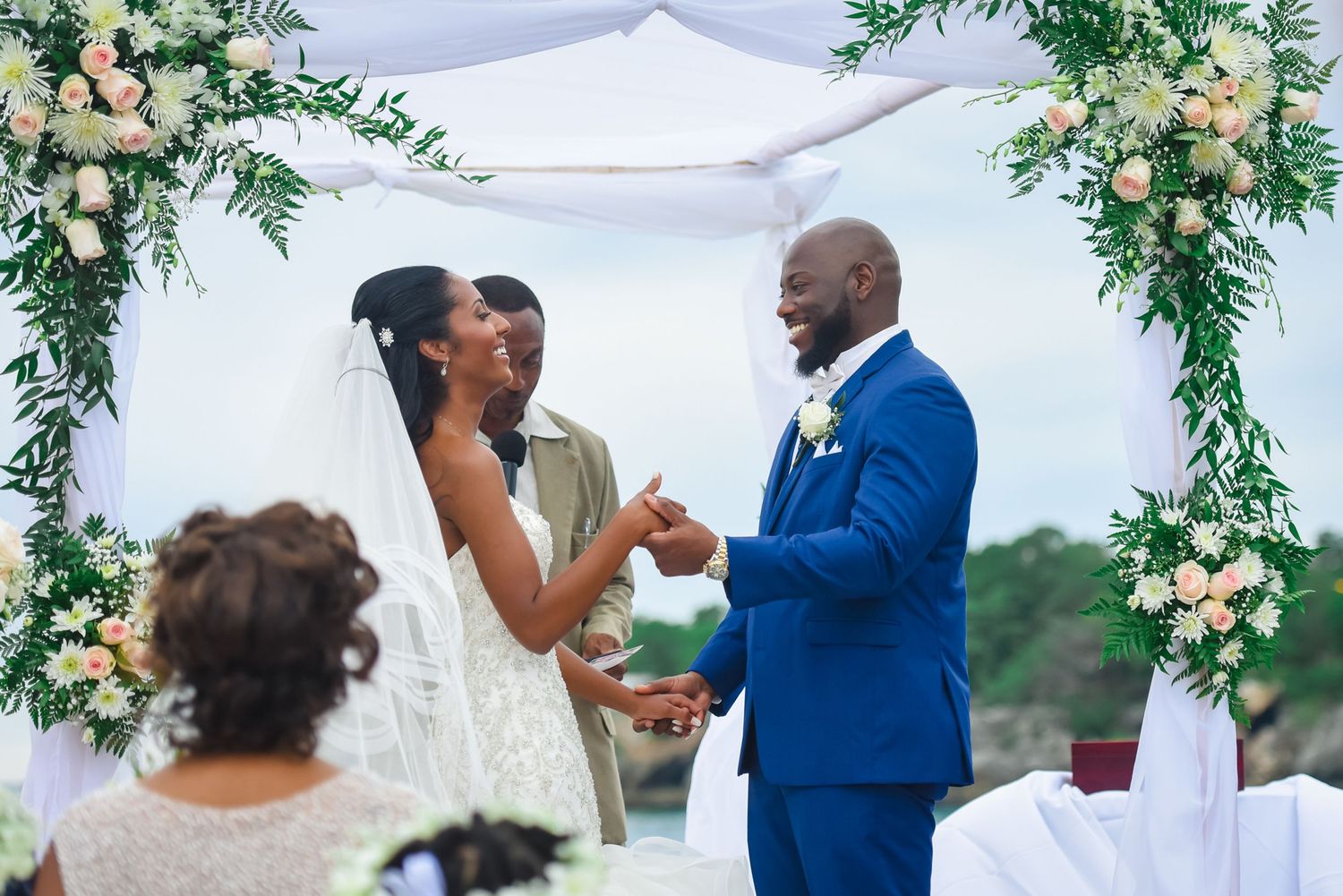 Celebratory moment during wedding ceremony beneath floral arch with peach and white flowers.