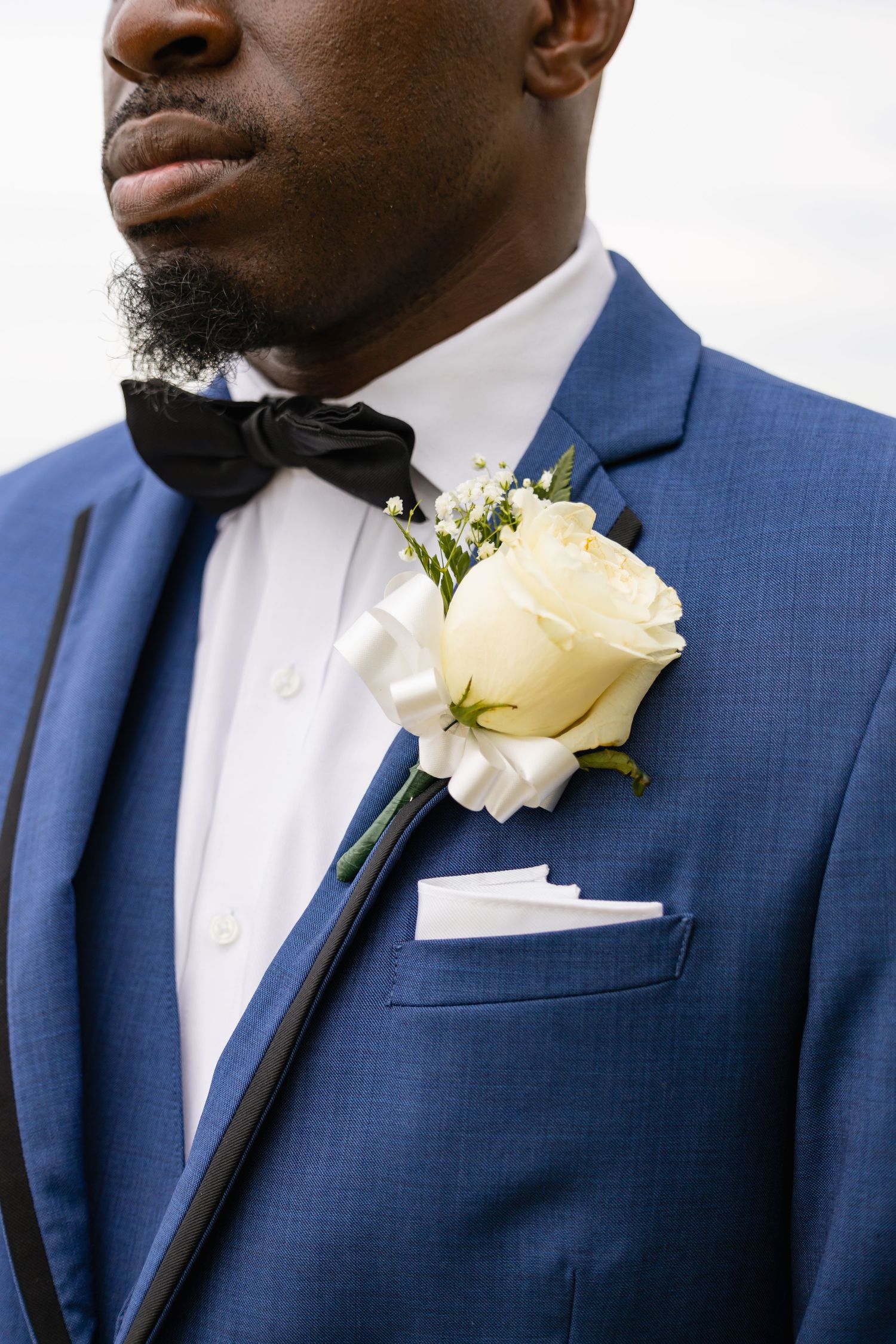 Close-up details of blue suit with white boutonniere and black bow tie.
