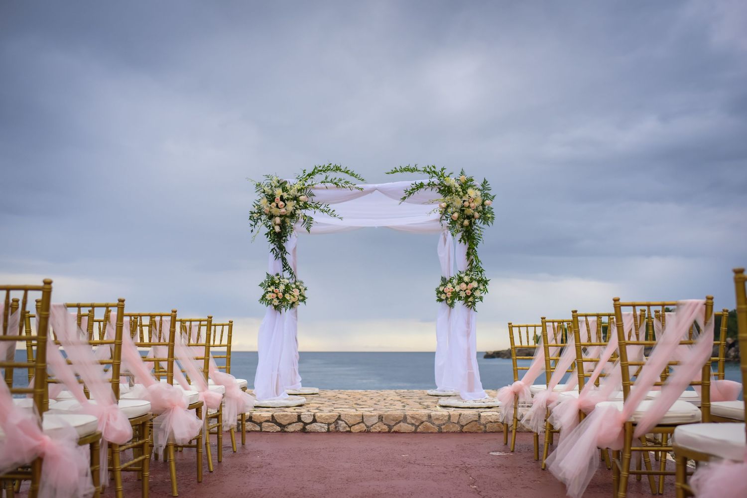 Elegant beach wedding ceremony setup with wooden chairs and floral decorations overlooking the ocean.