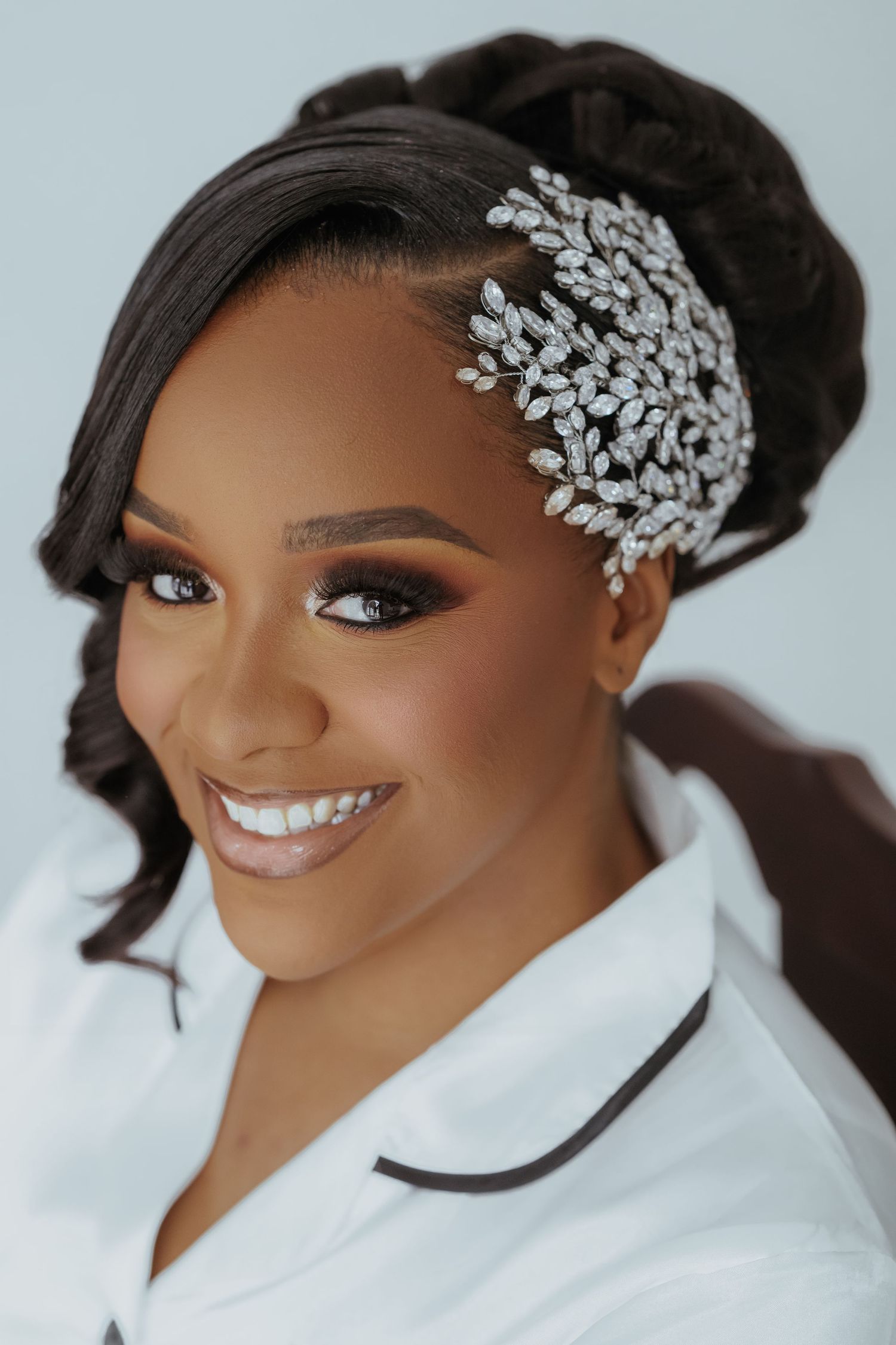Elegant bridal portrait showcasing a crystal hair accessory and flawless makeup against a white background.