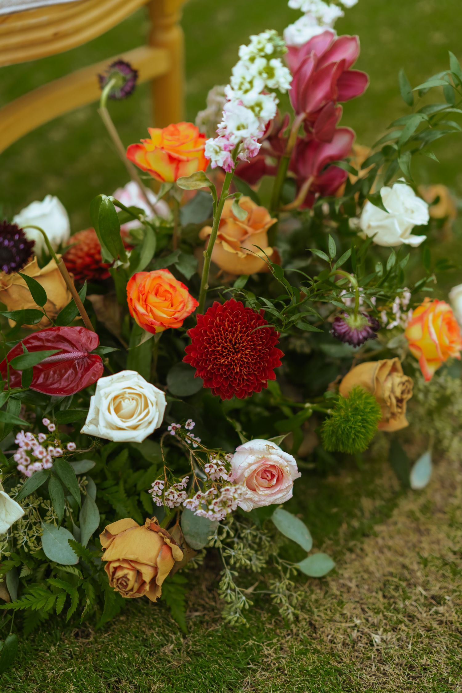 Colorful wedding floral arrangements with orange, white and red flowers displayed on mossy green ground.