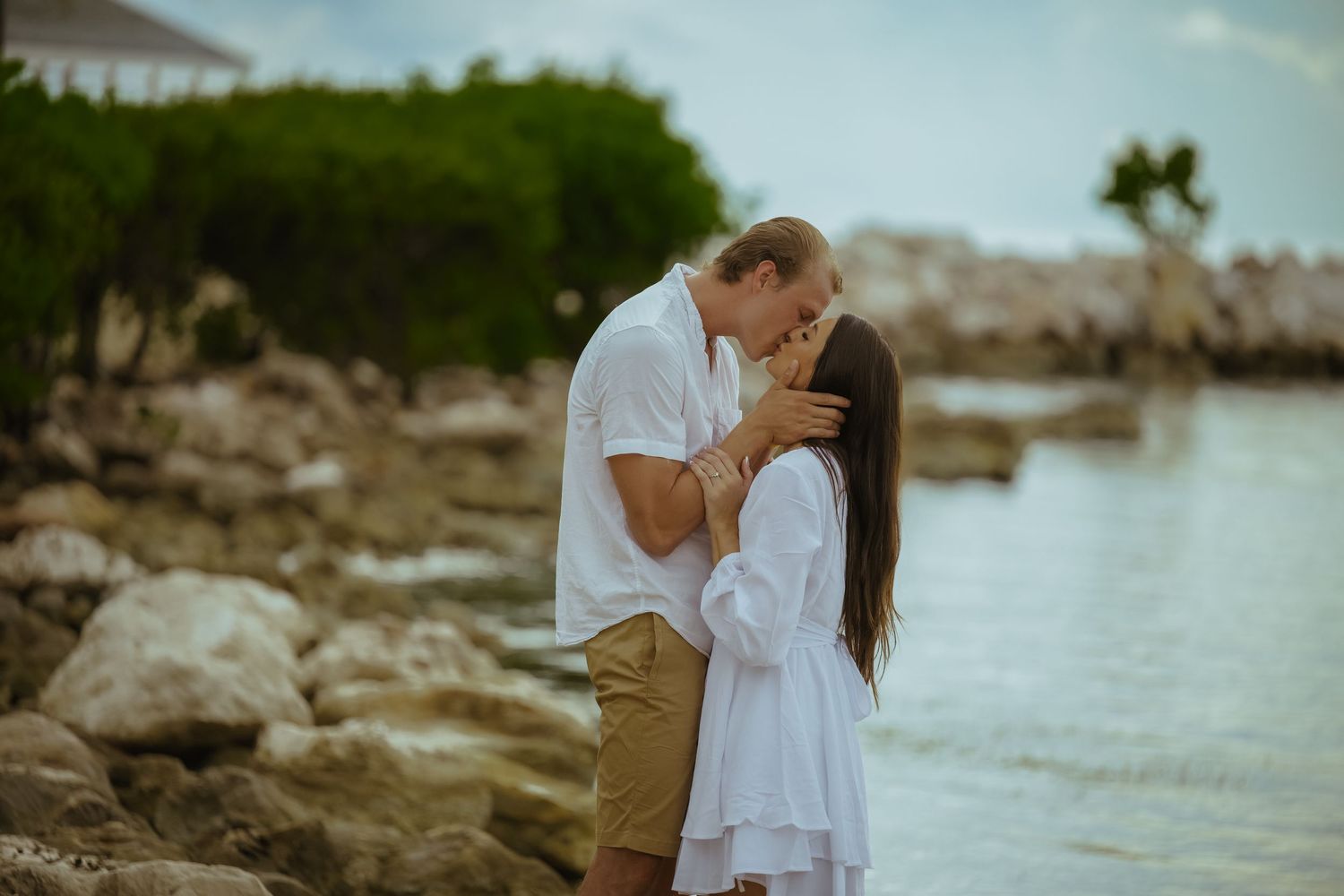 Couple posing for romantic photos by rocky coastline during golden hour.