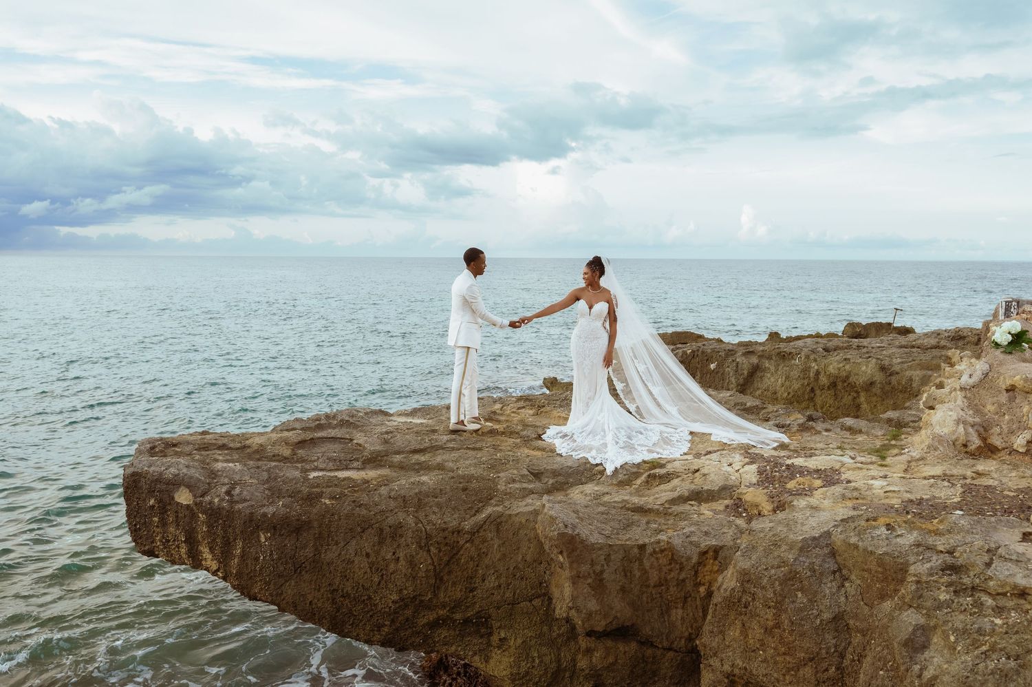 Newlyweds posing on dramatic rocky coastline overlooking the ocean.