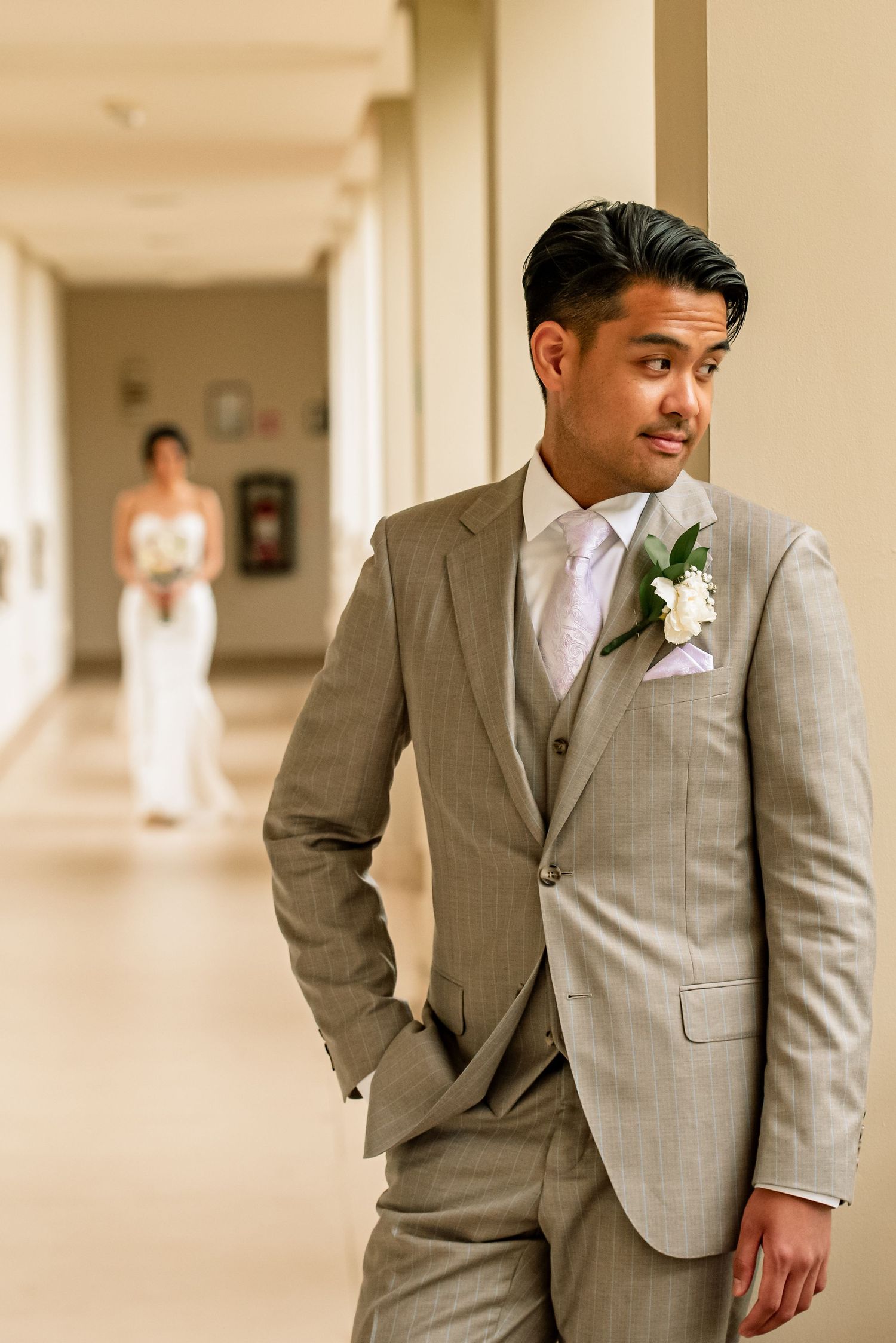 Wedding first look moment captured in a bright hallway with groom in gray suit.