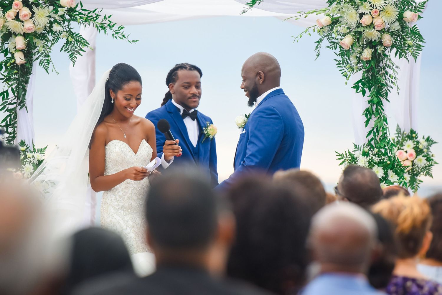 Wedding ceremony under elegant white tent decorated with peach flowers and green foliage.