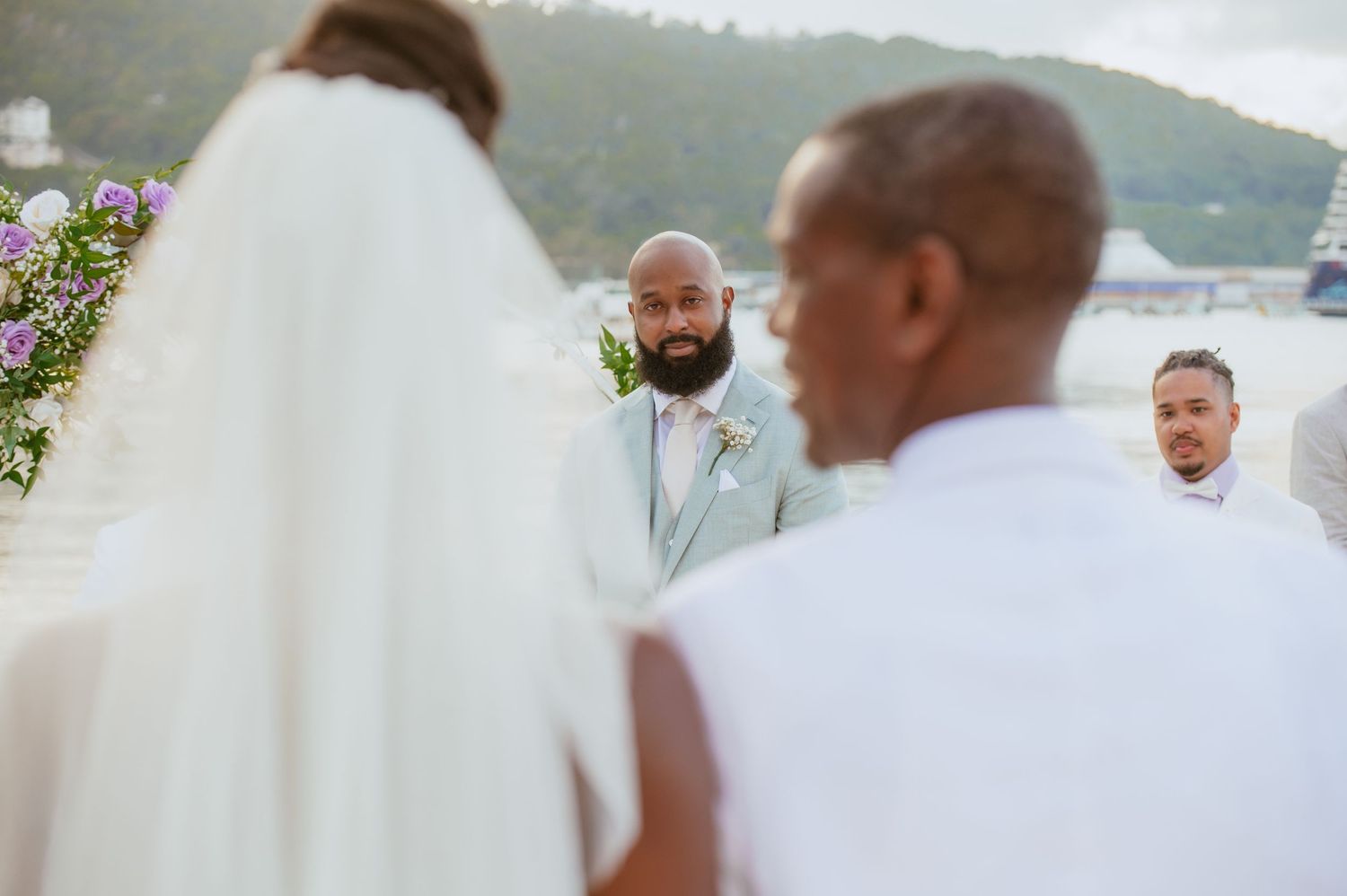 Wedding ceremony setup on a tropical beach with white decor and palm trees in the background.