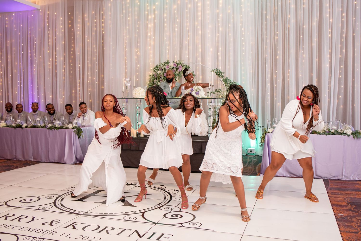 Group performs choreographed dance routine on custom monogrammed dance floor at wedding reception.