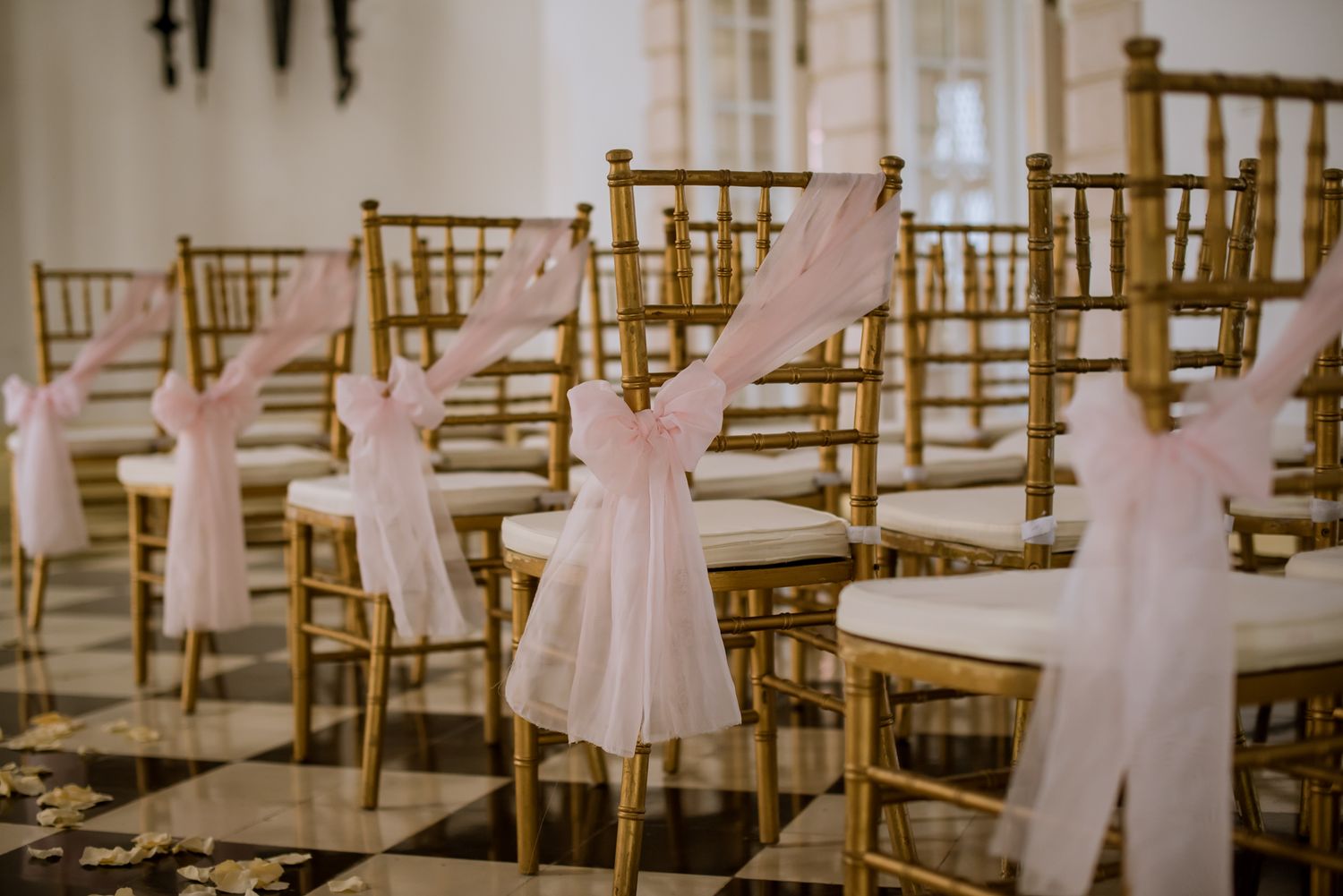 Wedding ceremony chairs decorated with white fabric sashes in an elegant ballroom setting.