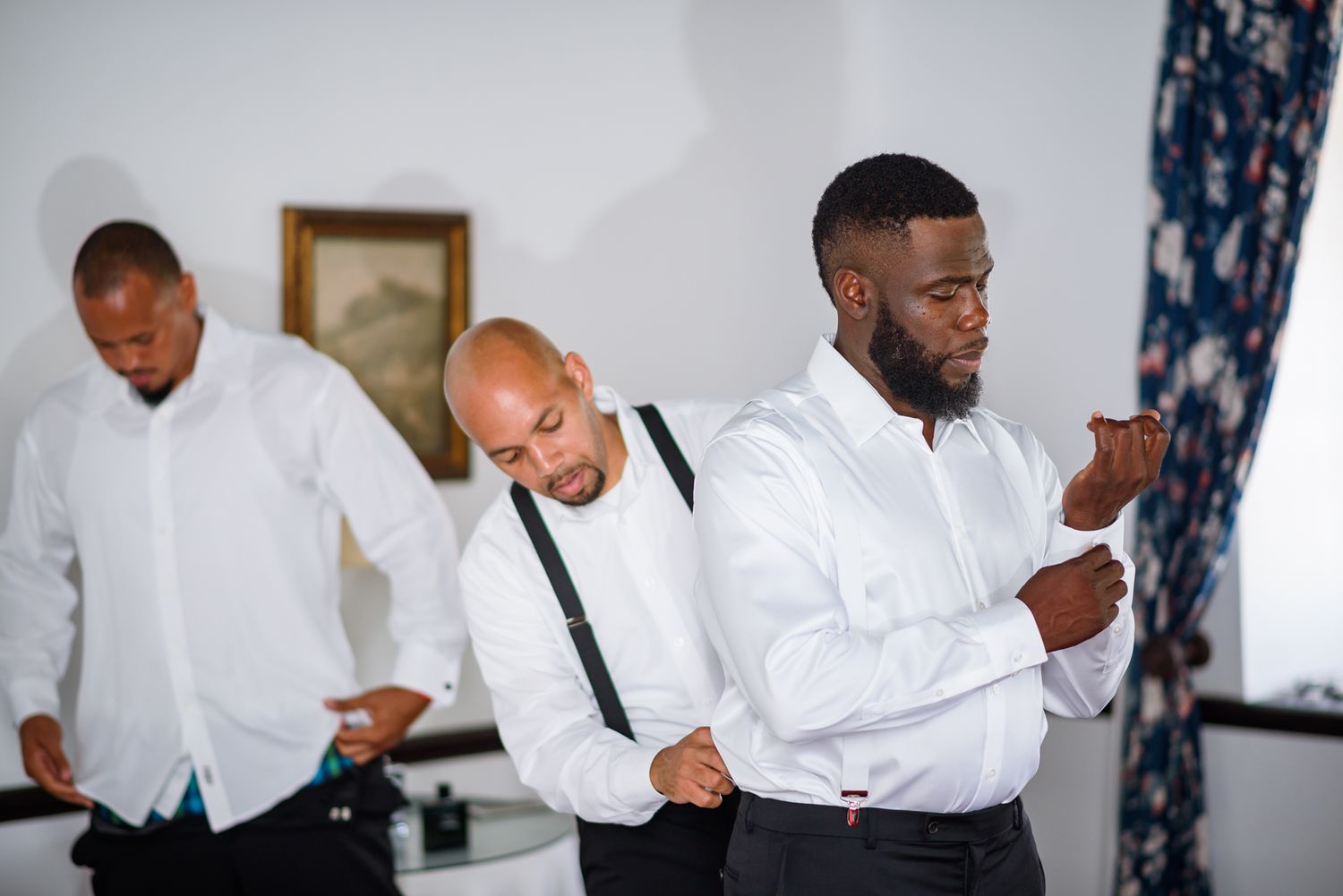 Wedding party members in white shirts and suspenders getting ready in an elegant room.