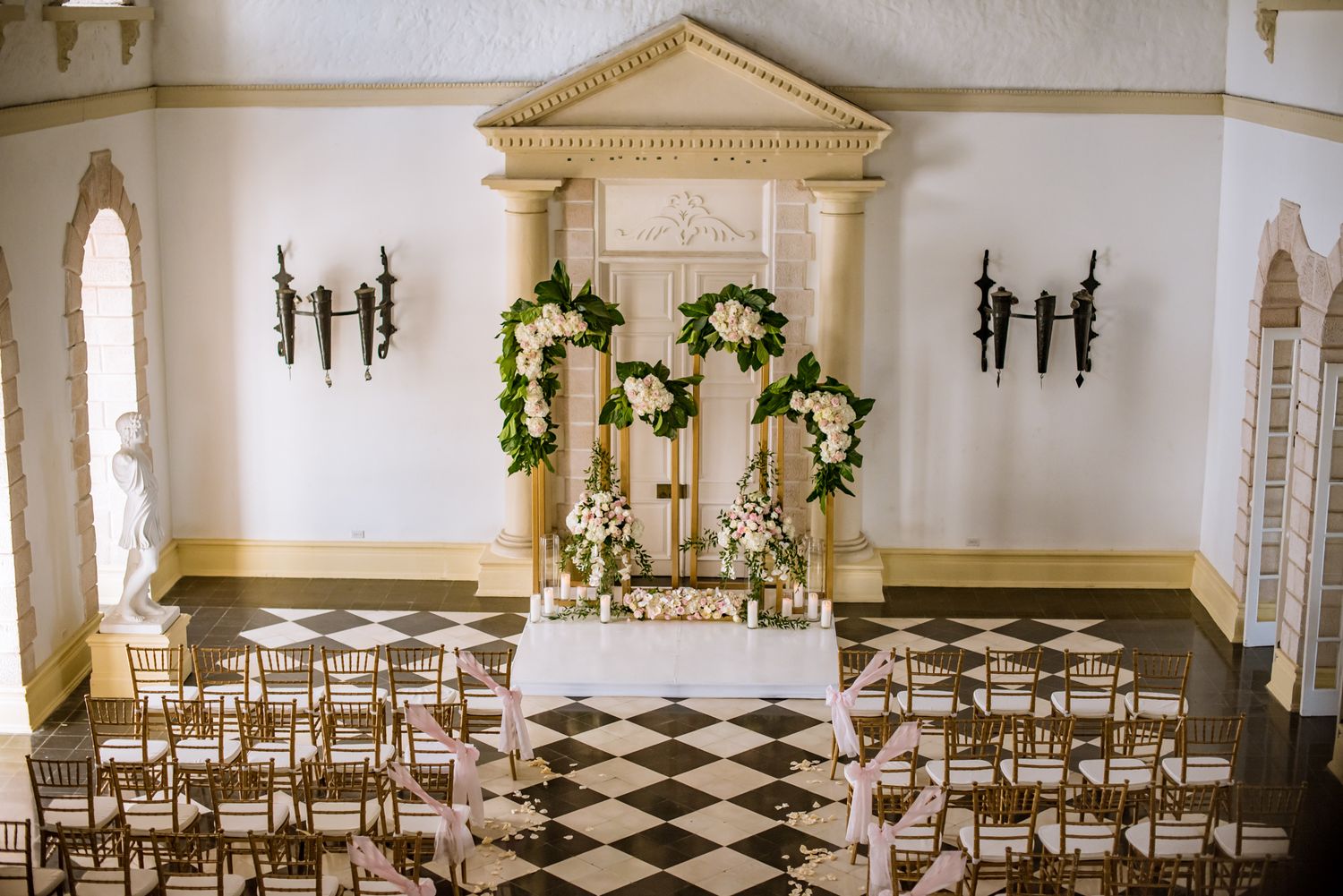 Grand wedding ceremony space with black and white checkered floor and rows of gold chairs.