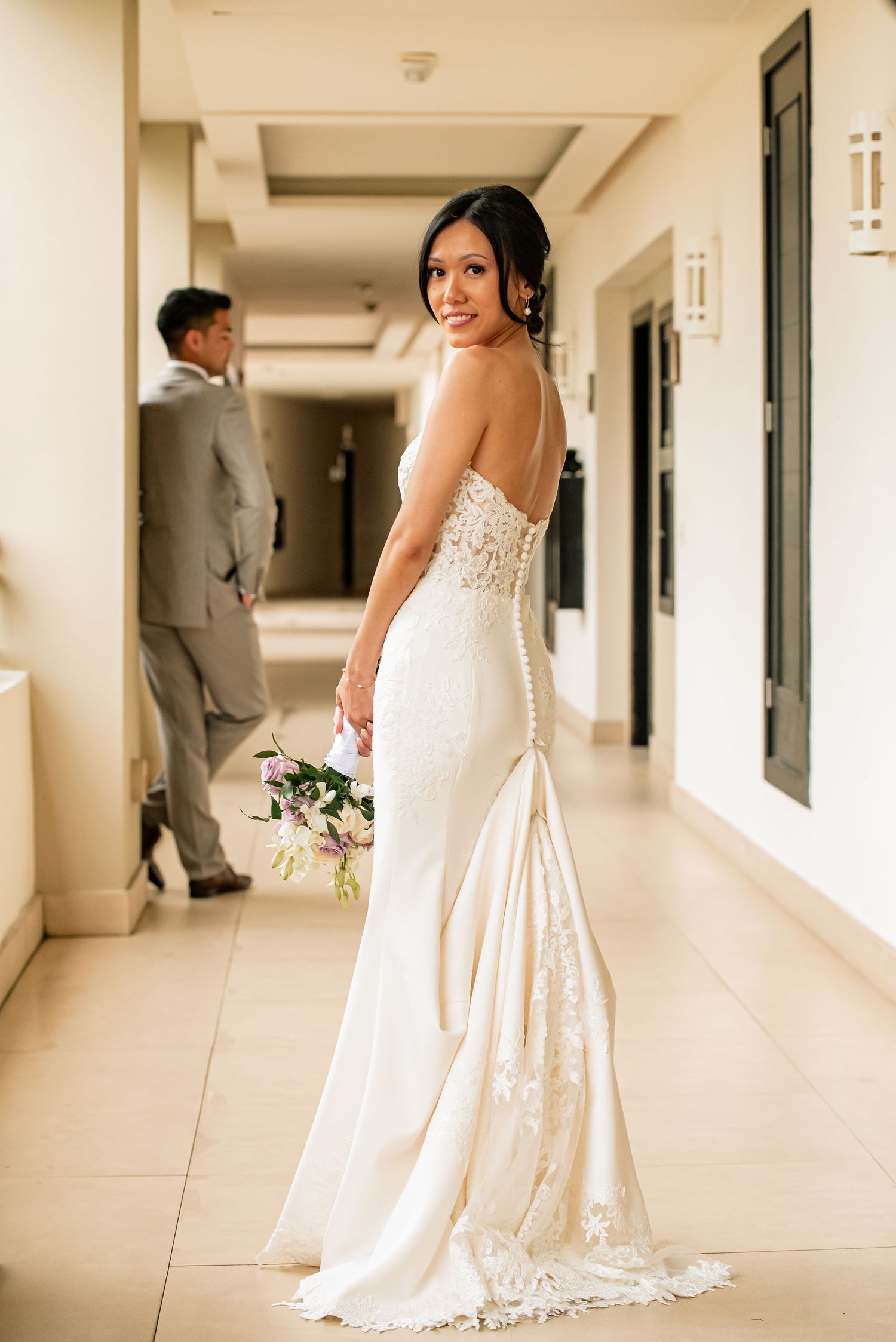 Bride in detailed white gown with train poses in hallway during first look photos.