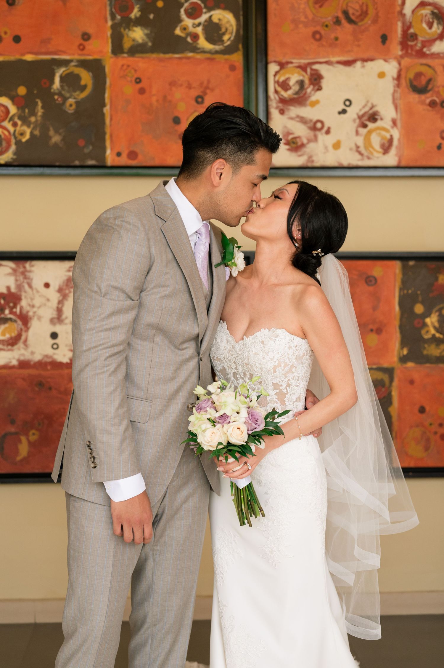 Wedding couple shares romantic kisses against vibrant orange abstract artwork.