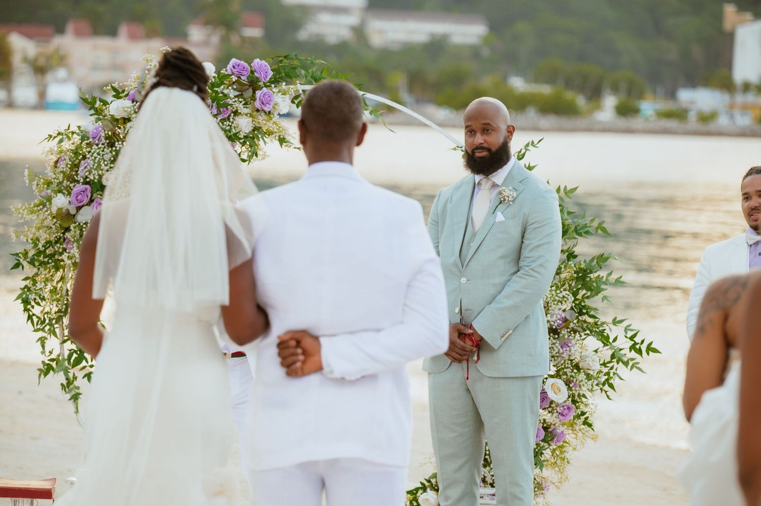 Elegant beachside wedding ceremony with floral decorations and guests in white attire.