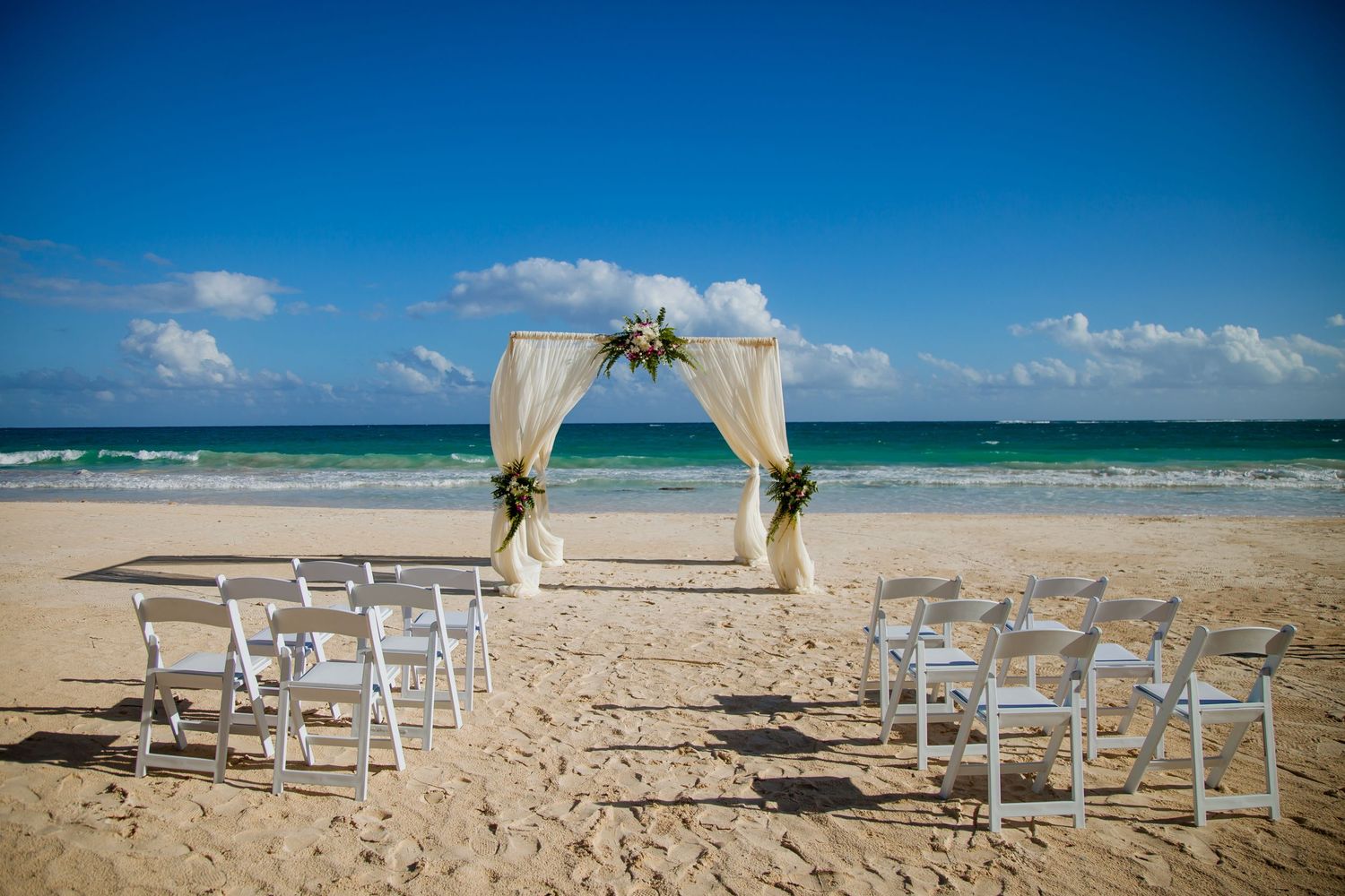 White chairs and fabric arch set up for beach wedding ceremony with ocean view.