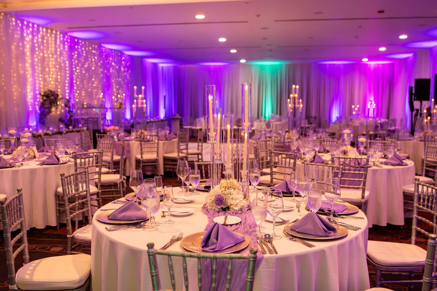 Elegant wedding reception tables with purple and white decor under dramatic lighting.
