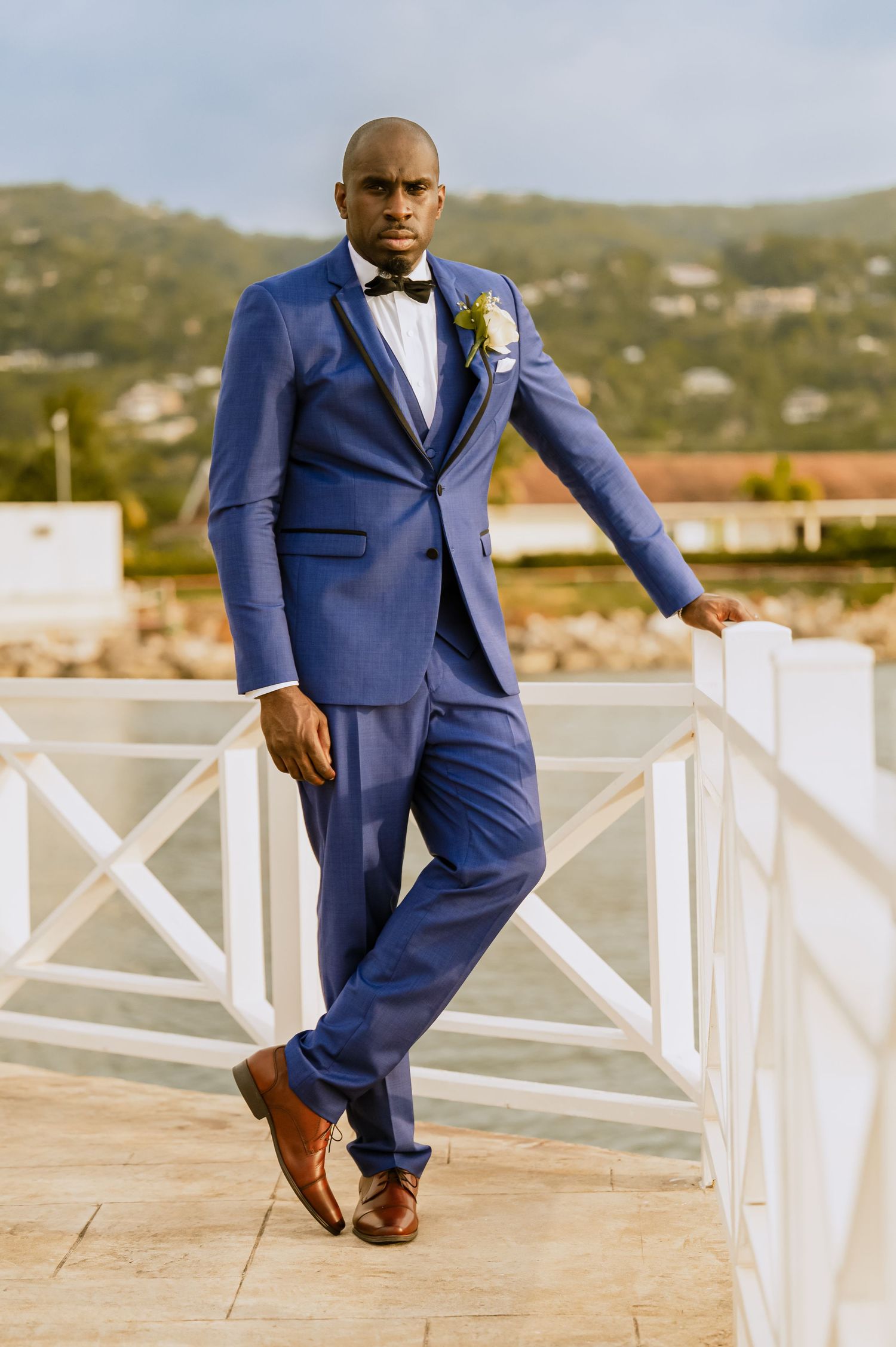 Groom in royal blue suit poses elegantly against mountain landscape.
